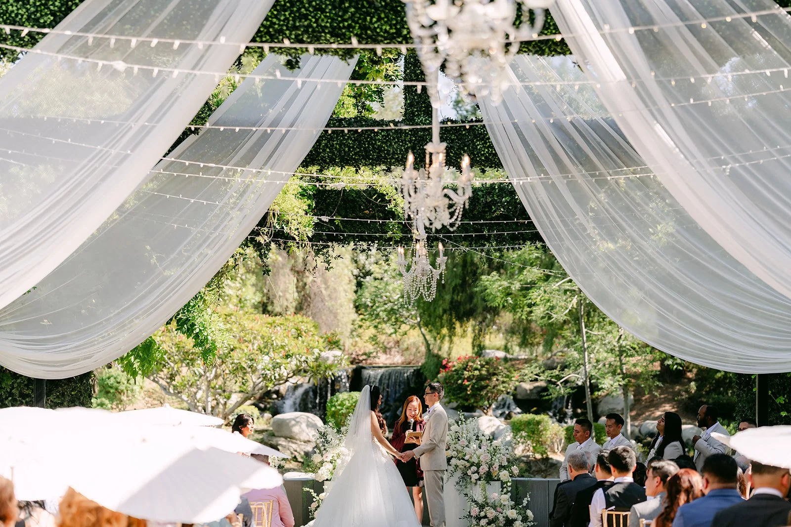Guests seated under the draped pergola and chandeliers for the ceremony.