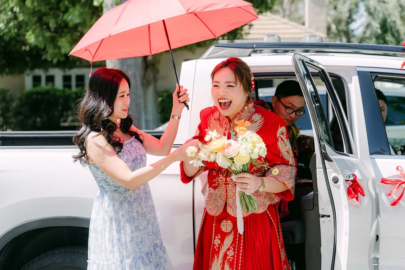 A red umbrella shading the bride as she steps toward the car.
