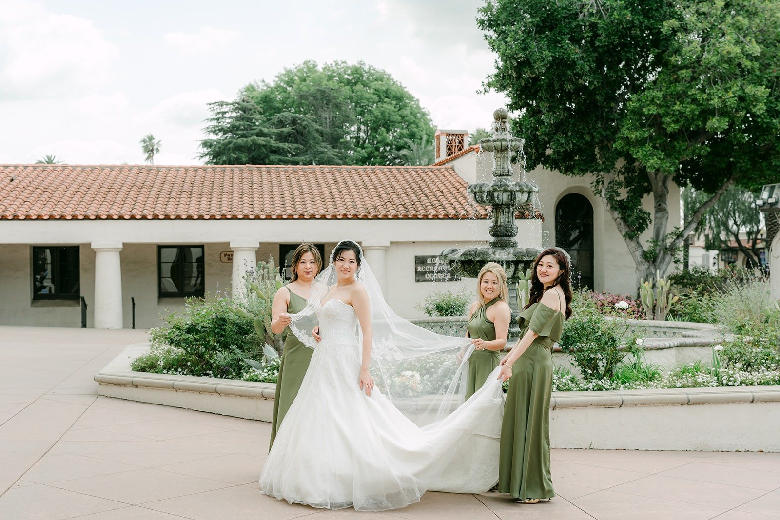 Eunice and her bridesmaids in olive green spread out her veil on the plaza