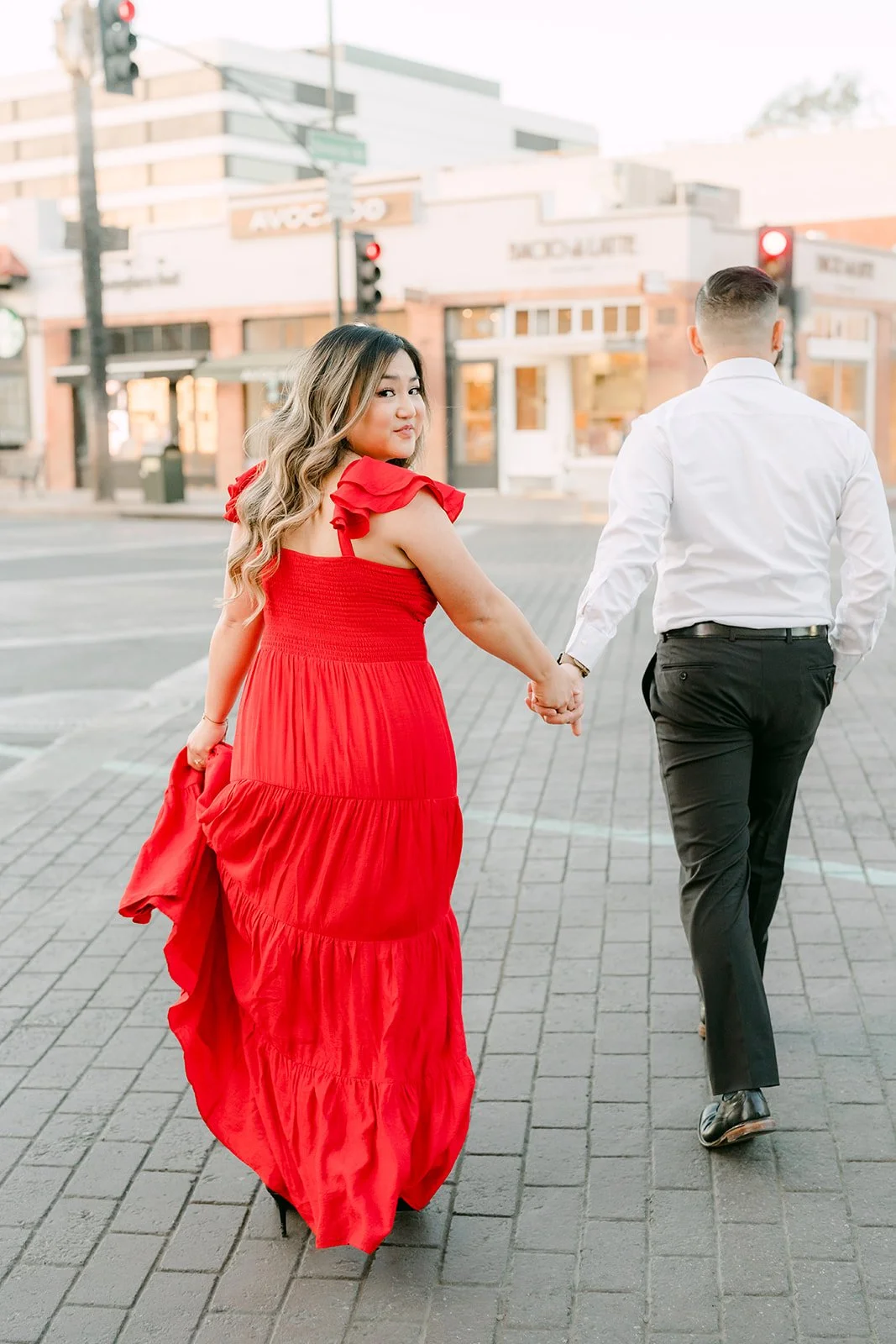 Linh pulls Ankush across the intersection, her red dress flowing.