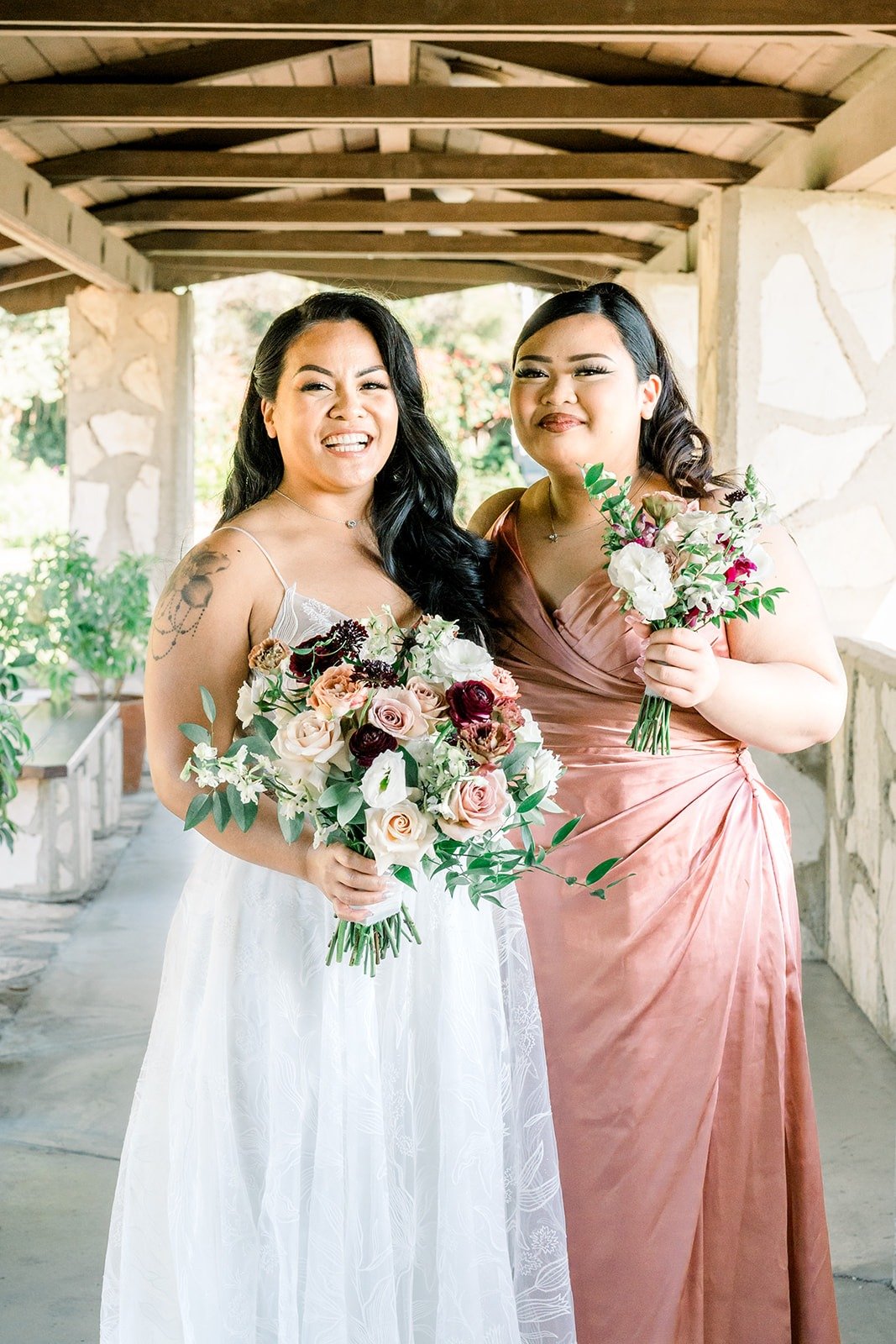Betsy shares a laugh with a bridesmaid holding their bouquets, photographed by One and Only Production