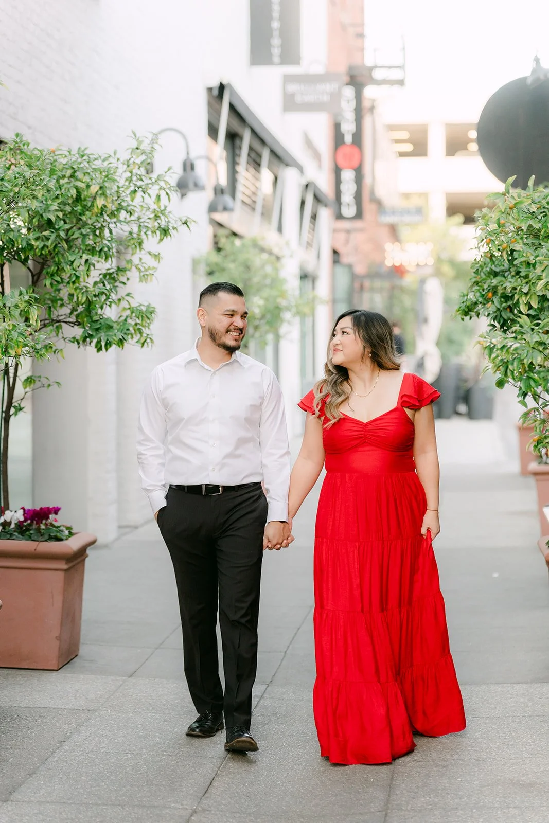 Linh and Ankush walk hand in hand down a paseo lined with planters.