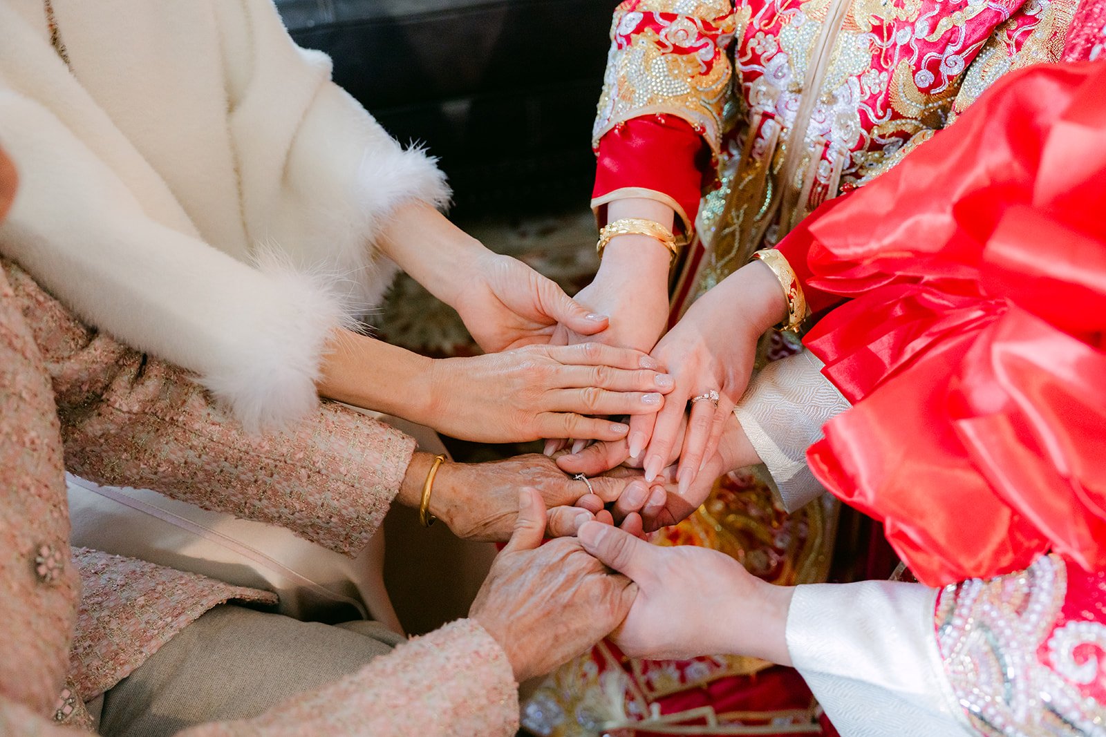 Family members' hands gathered around the bride's wrist as a gold bangle goes on.