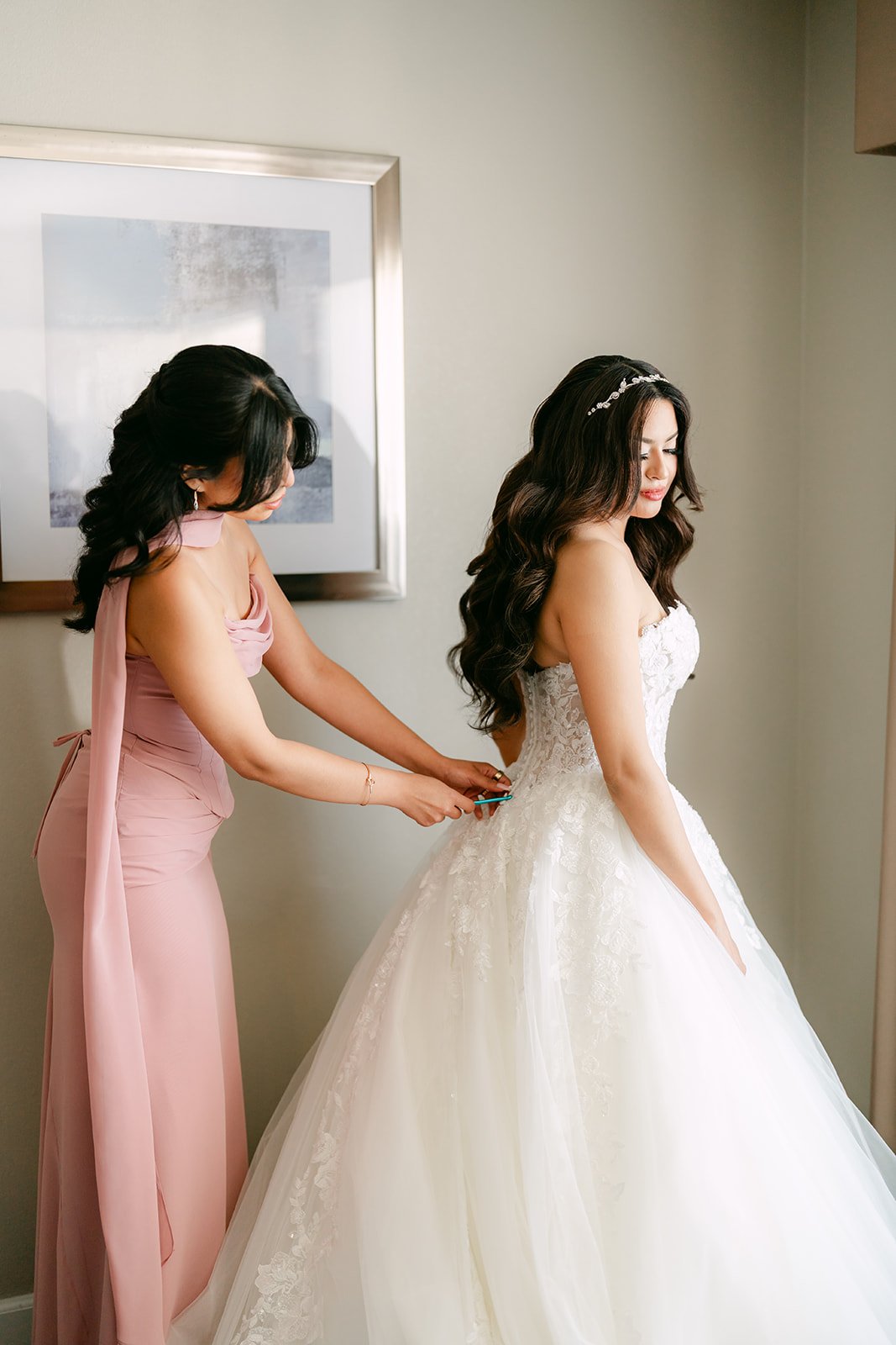 A bridesmaid in dusty pink lacing up Sandra's ball gown.