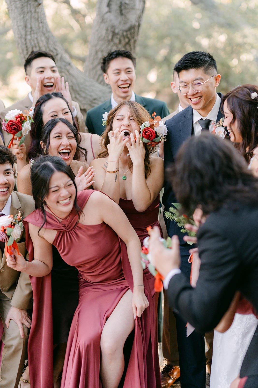 Bridesmaids and groomsmen crowd in laughing for a close group photo