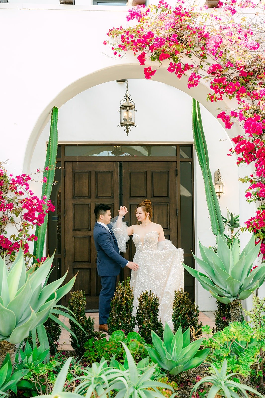 Joanna and Jerrick under the arched entry lined with agave and pink bougainvillea