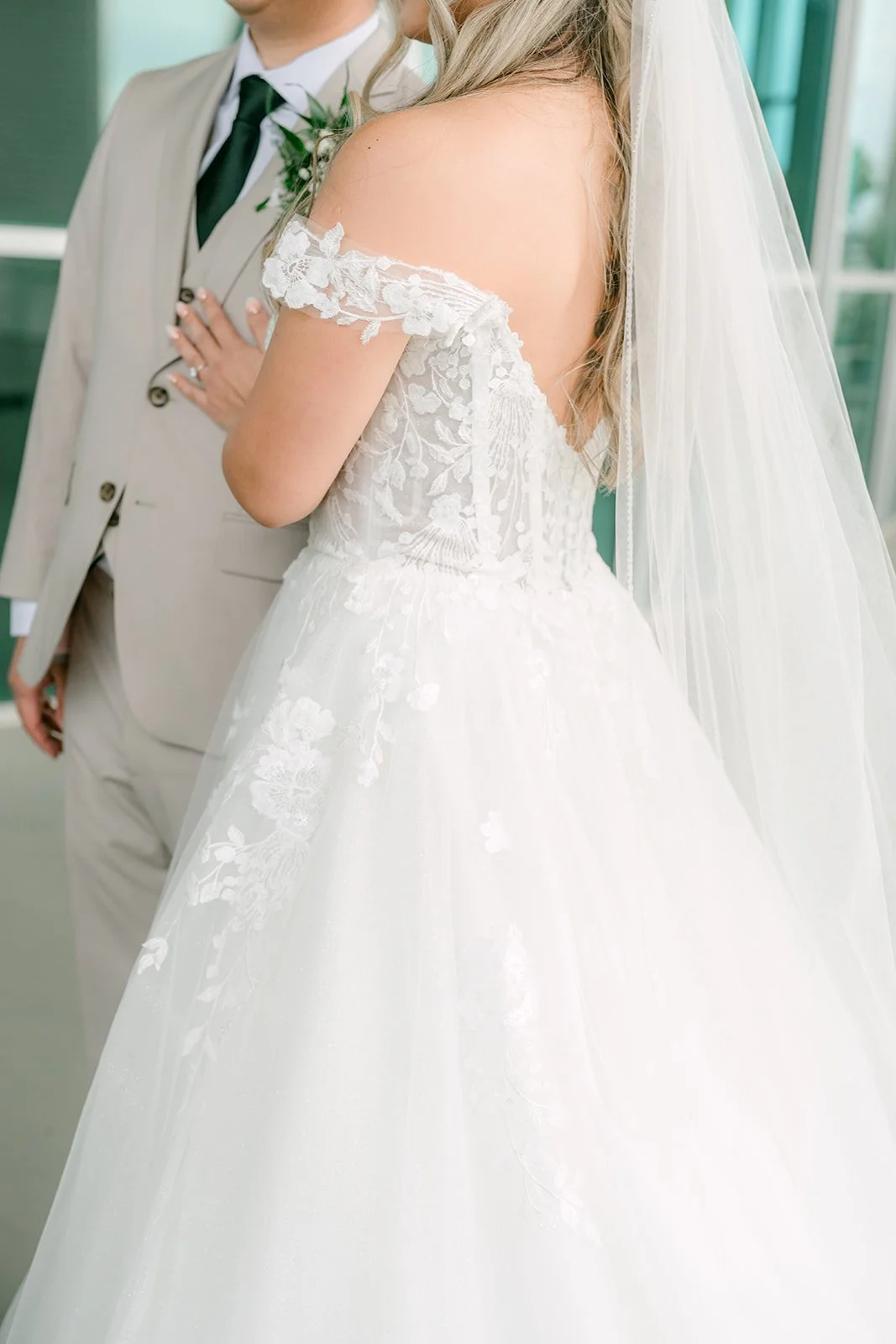 Detail of the bride's off the shoulder lace gown and veil beside the groom