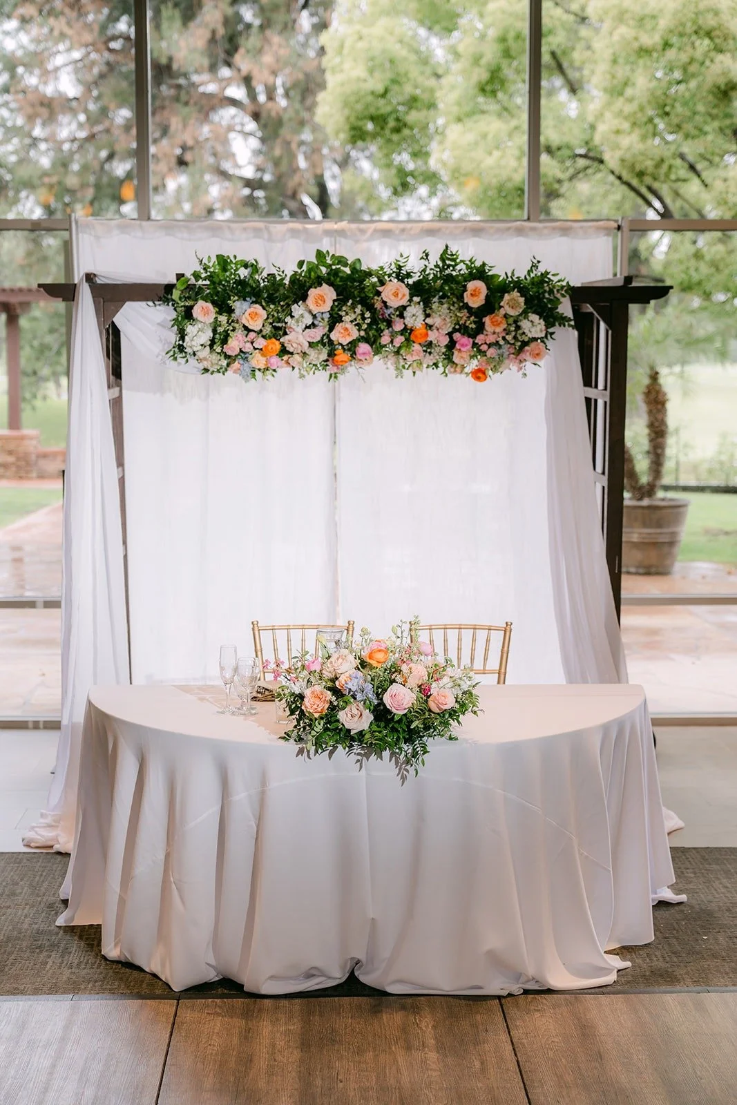 The sweetheart table under a white draped arch with flowers
