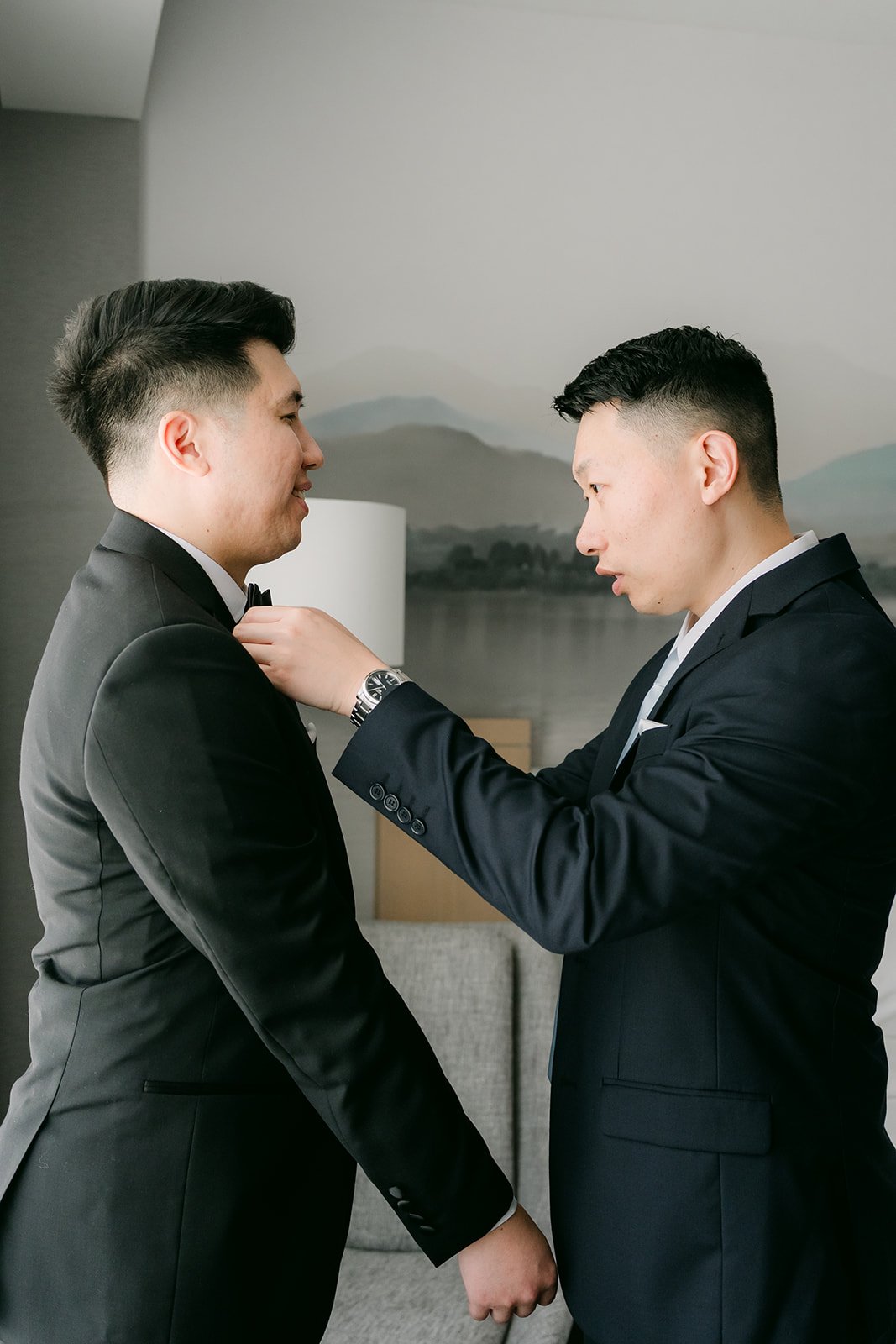 A groomsman helping San with his tuxedo jacket.