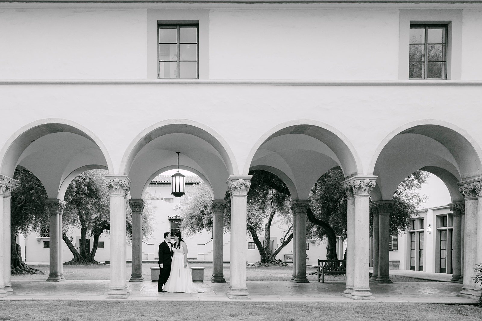 A black and white view of Saira and Matthew standing between the arches