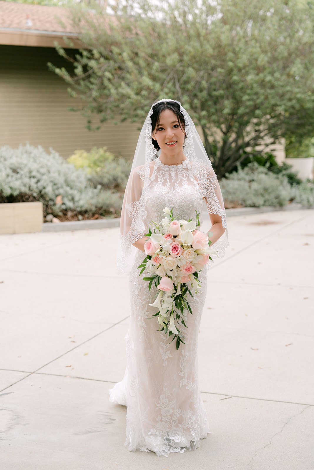 Elaine holding her pink and white bouquet in her lace gown.