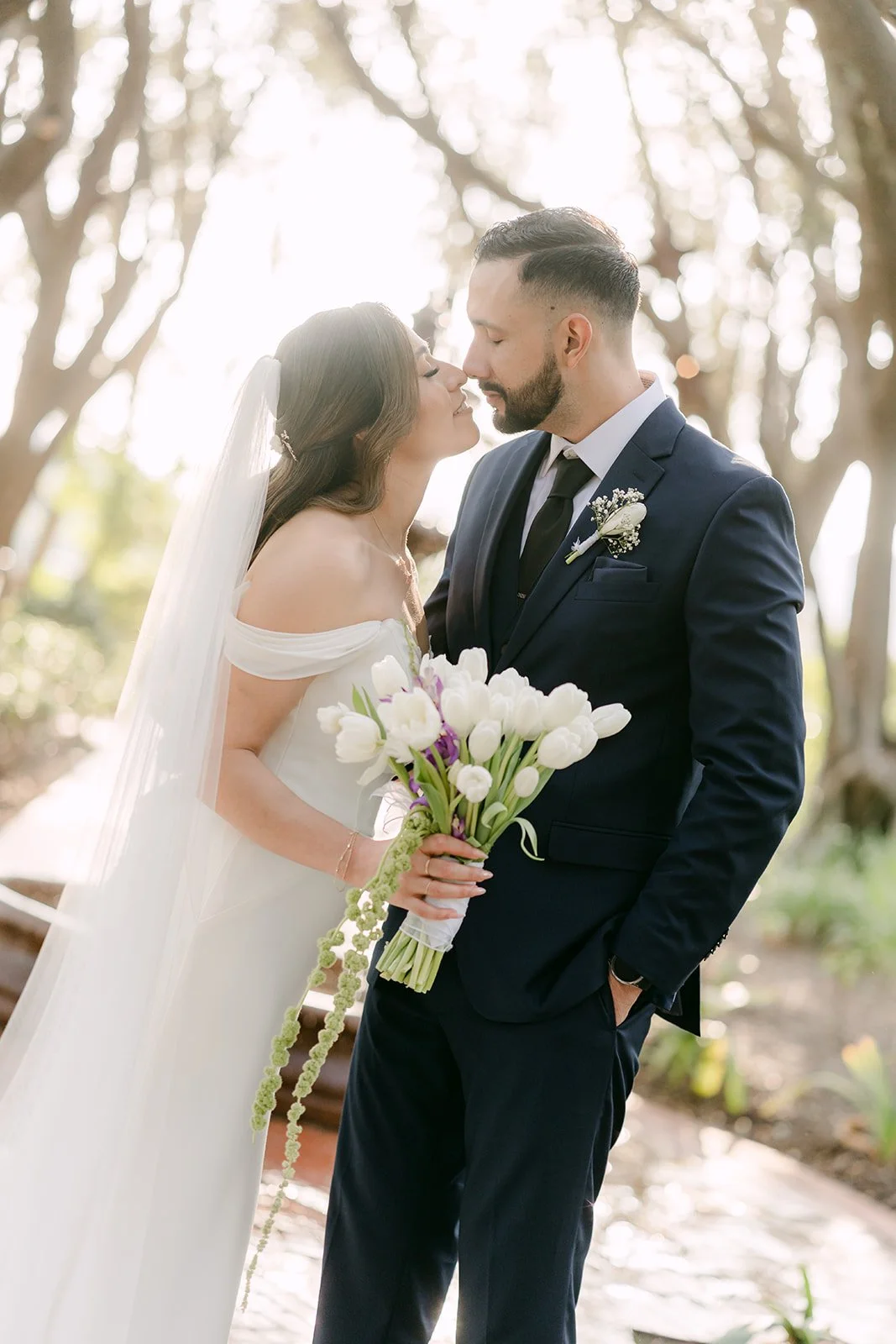Danny leaning in to kiss Mariana's cheek, her bouquet in hand