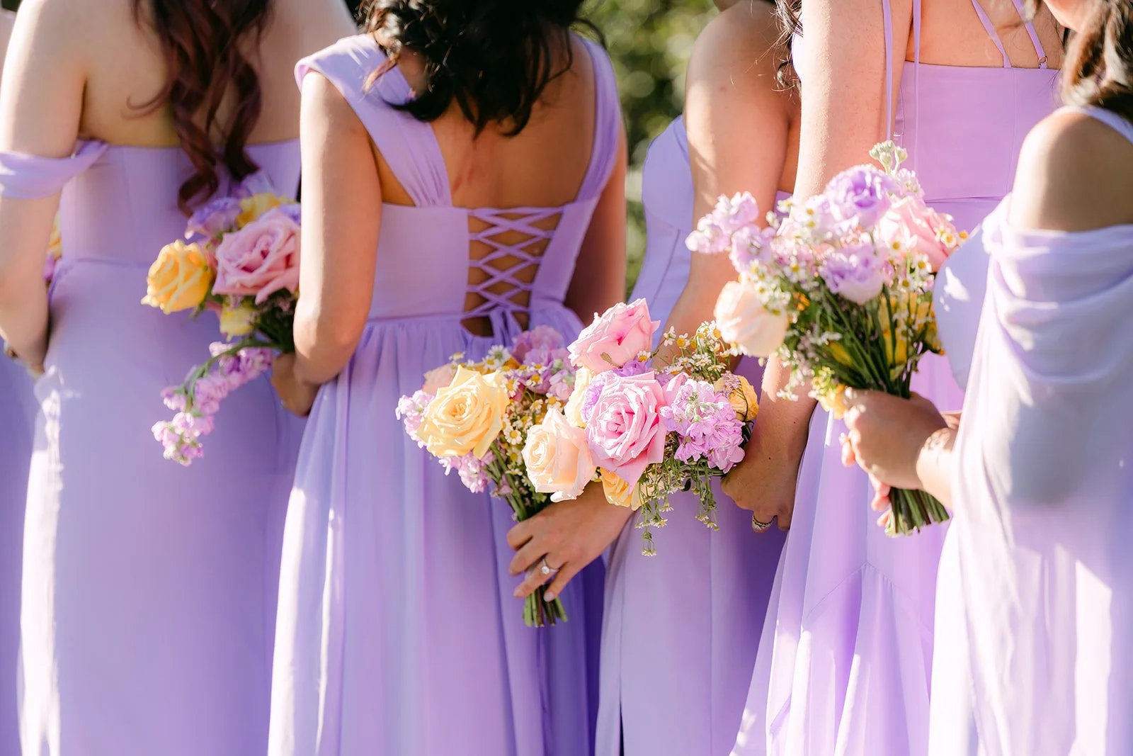 Lace-up backs of the bridesmaids' lilac dresses and their bouquets.
