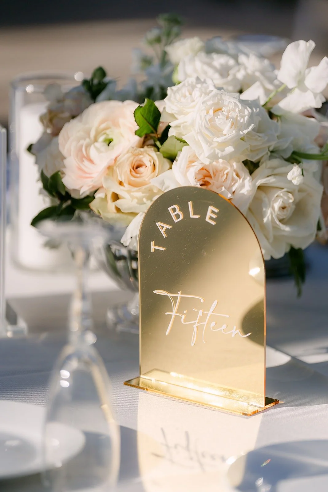 A gold acrylic table number in front of ivory roses