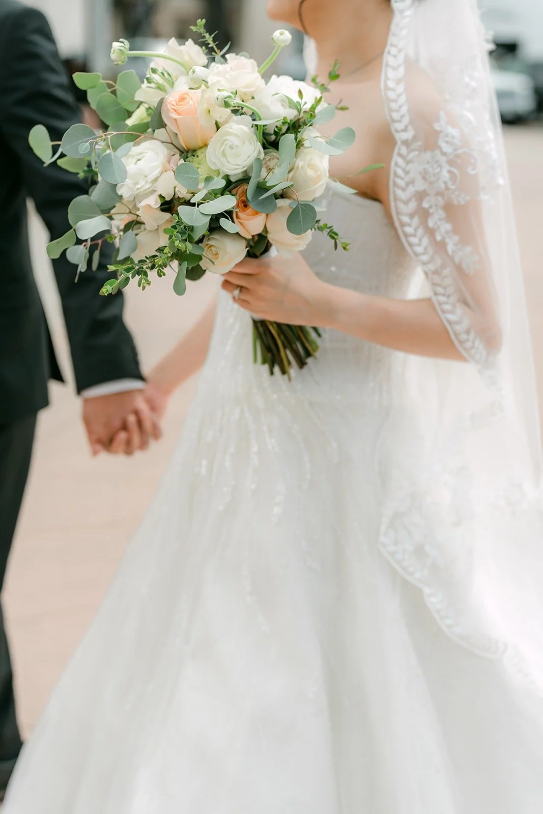 Eunice and Eric holding hands, her bouquet of white and blush roses in front