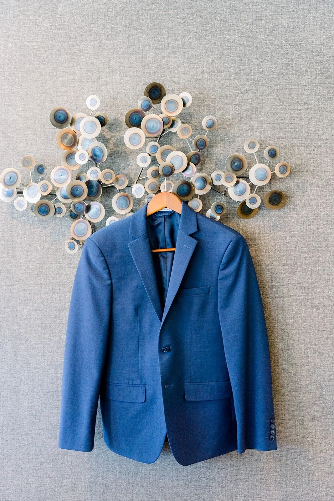 Alex's navy suit jacket hanging against a textured wall