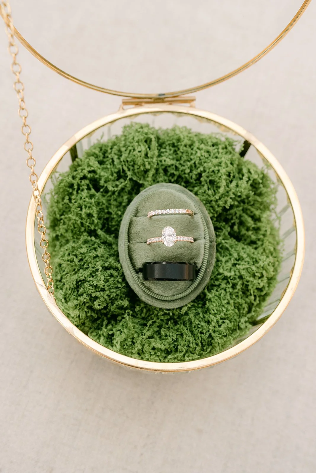 Wedding rings in a green velvet box on moss inside a gold ring cage