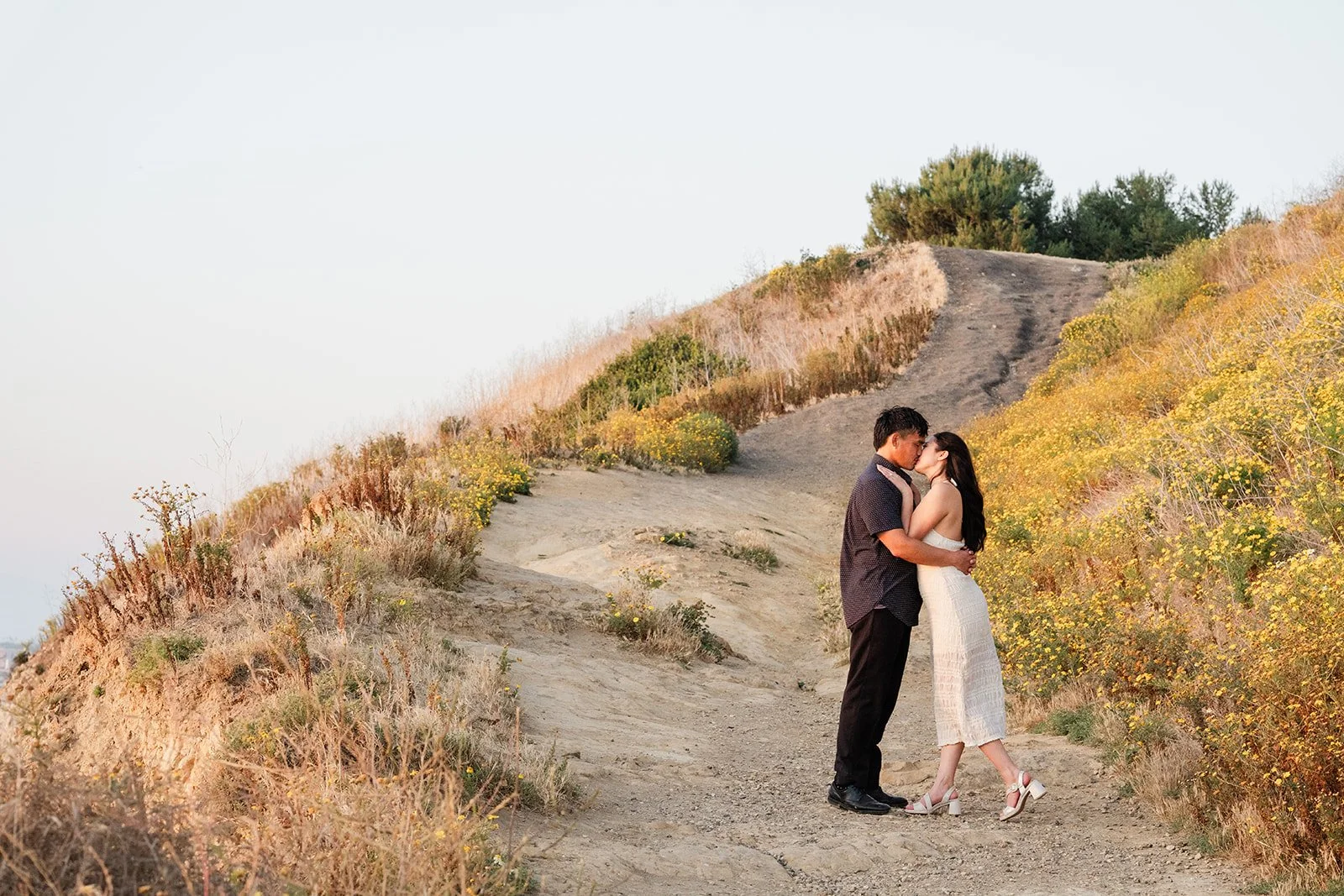 Victoria and Andrew stand on the coastline trail among the golden grasses.