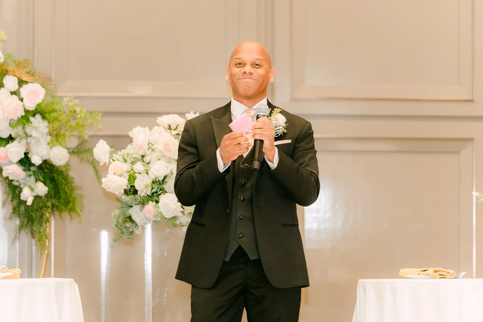 A guest in a tuxedo giving a toast in front of the sweetheart table florals