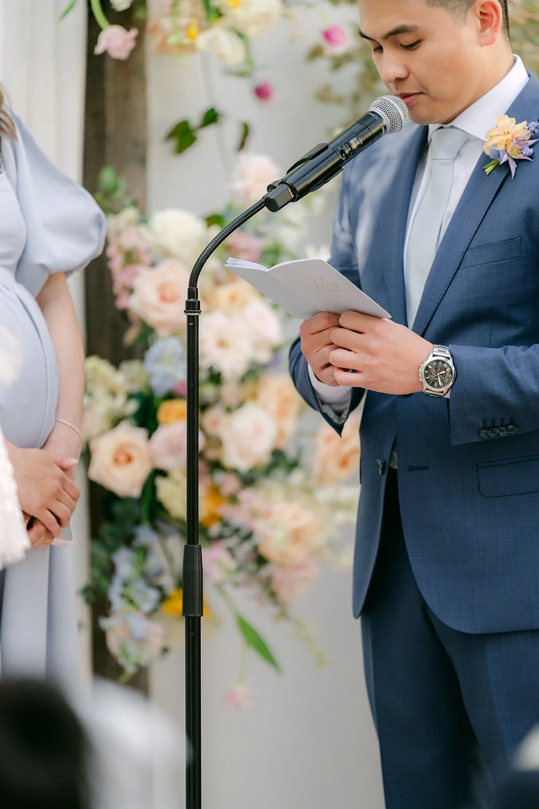 Jerrick reading his vows into the microphone beside pastel florals