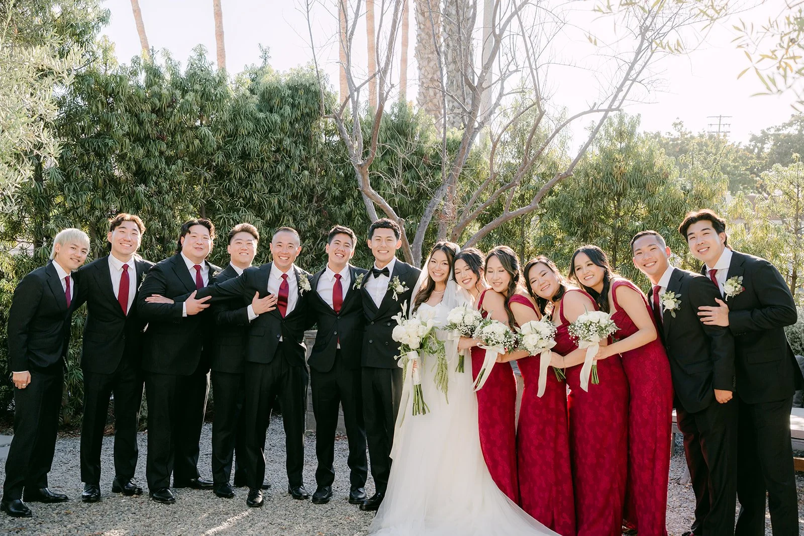Full wedding party in burgundy and black tuxedos in the garden at The Harper