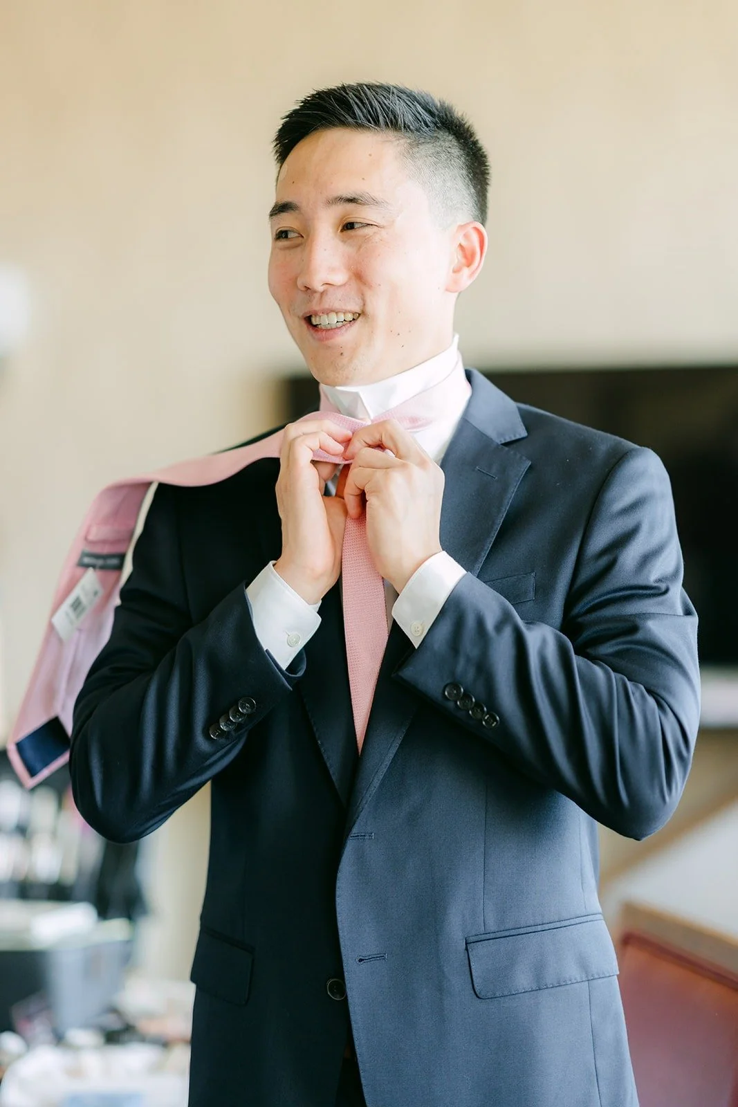 A groomsman in a navy suit fixing his tie