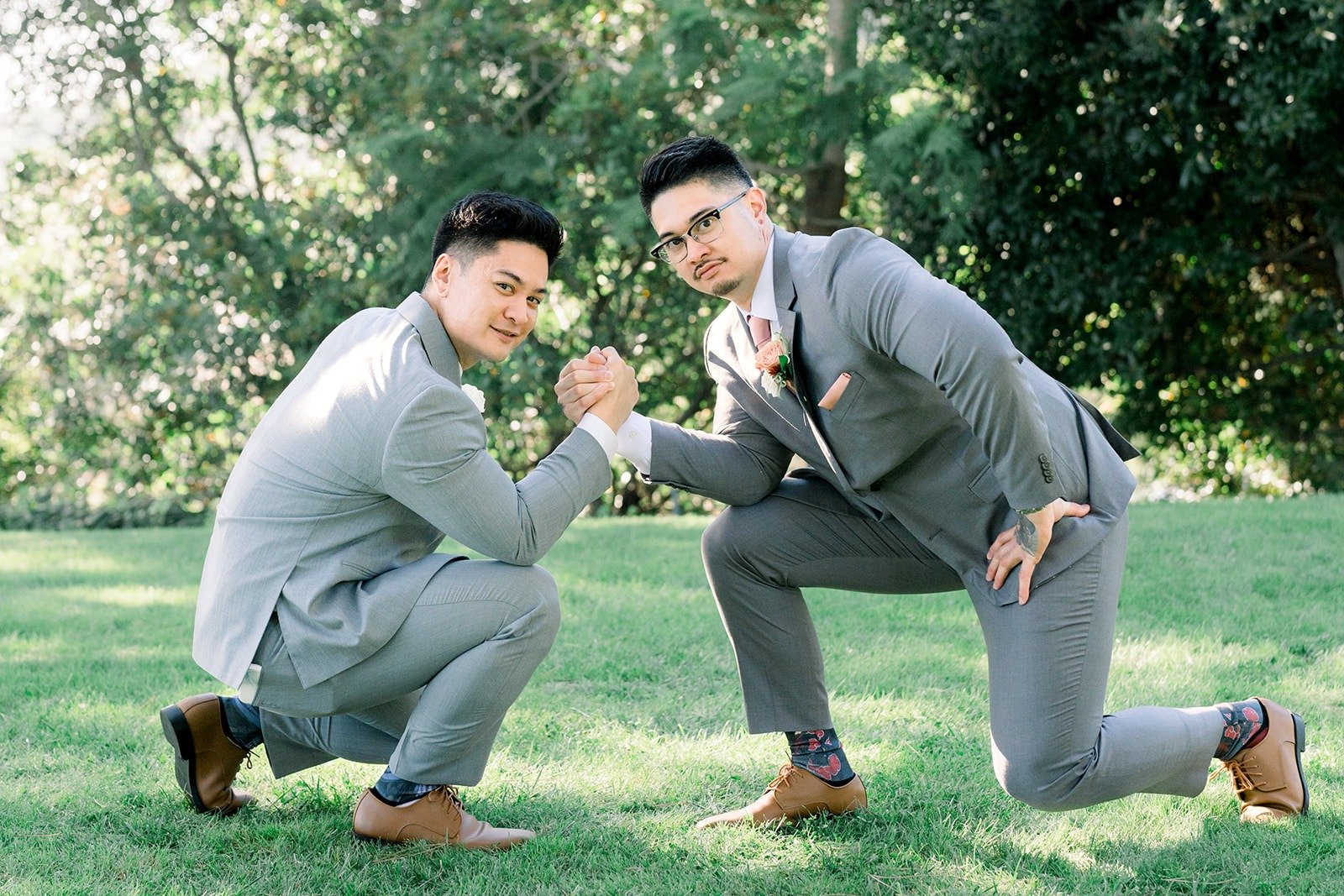 Mikey and a groomsman kneel and clown around on the grass, photographed by One and Only Production