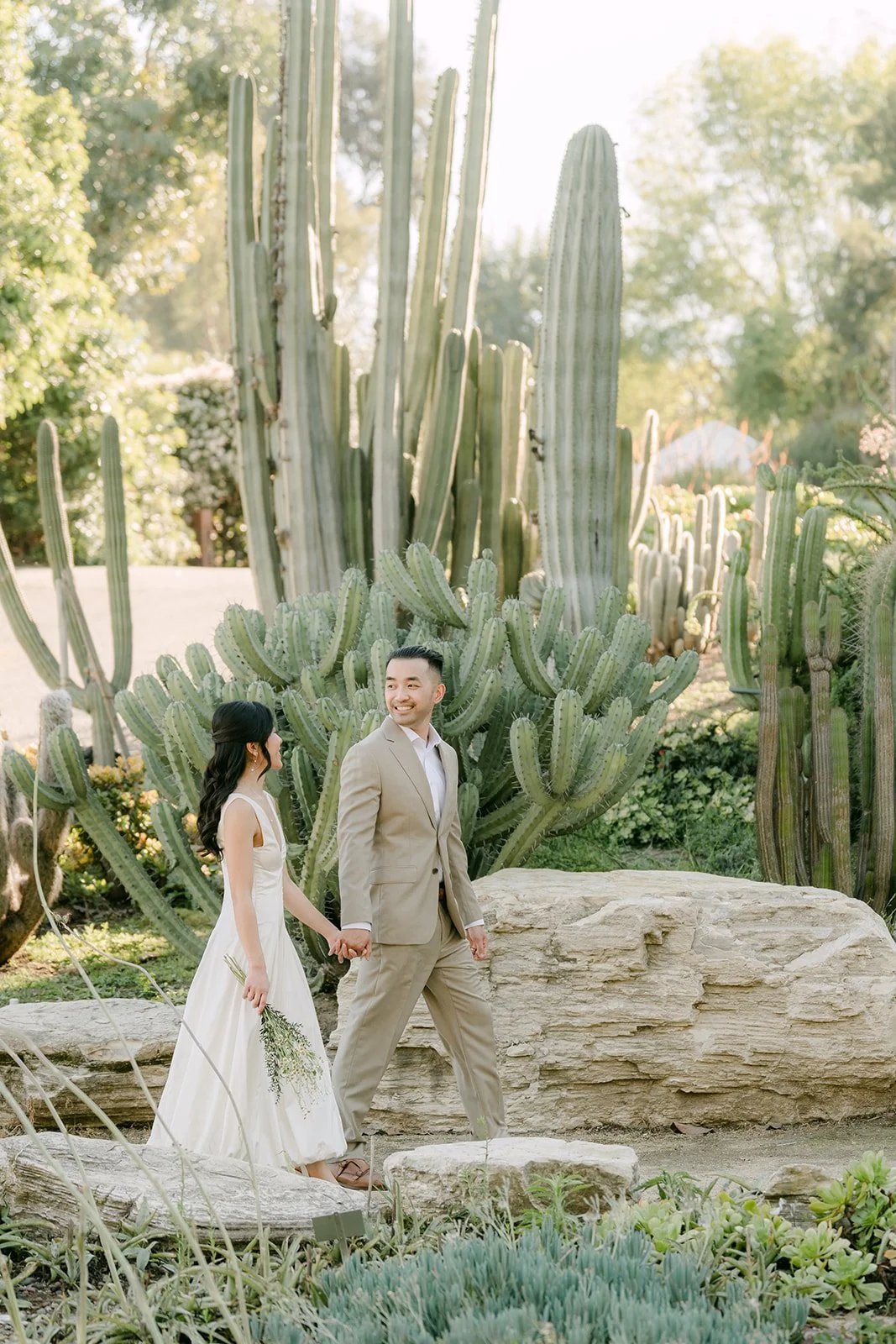 Kim and Vincent holding hands among towering cacti and sandstone boulders.