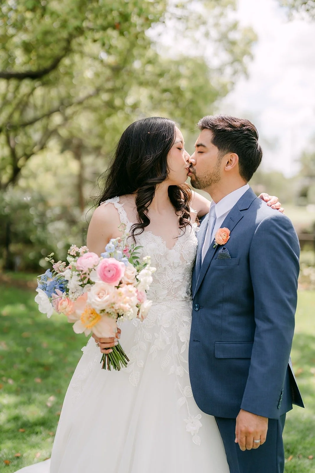 Natalie and Mark kissing on the lawn with her bouquet at her side
