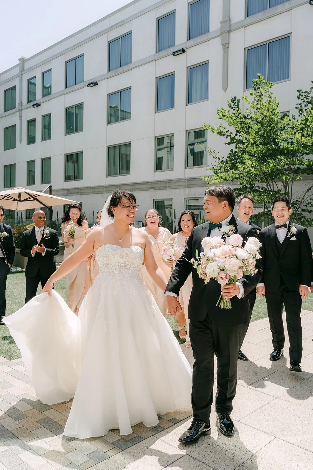 Stella and James walking hand in hand toward the camera with the wedding party behind them