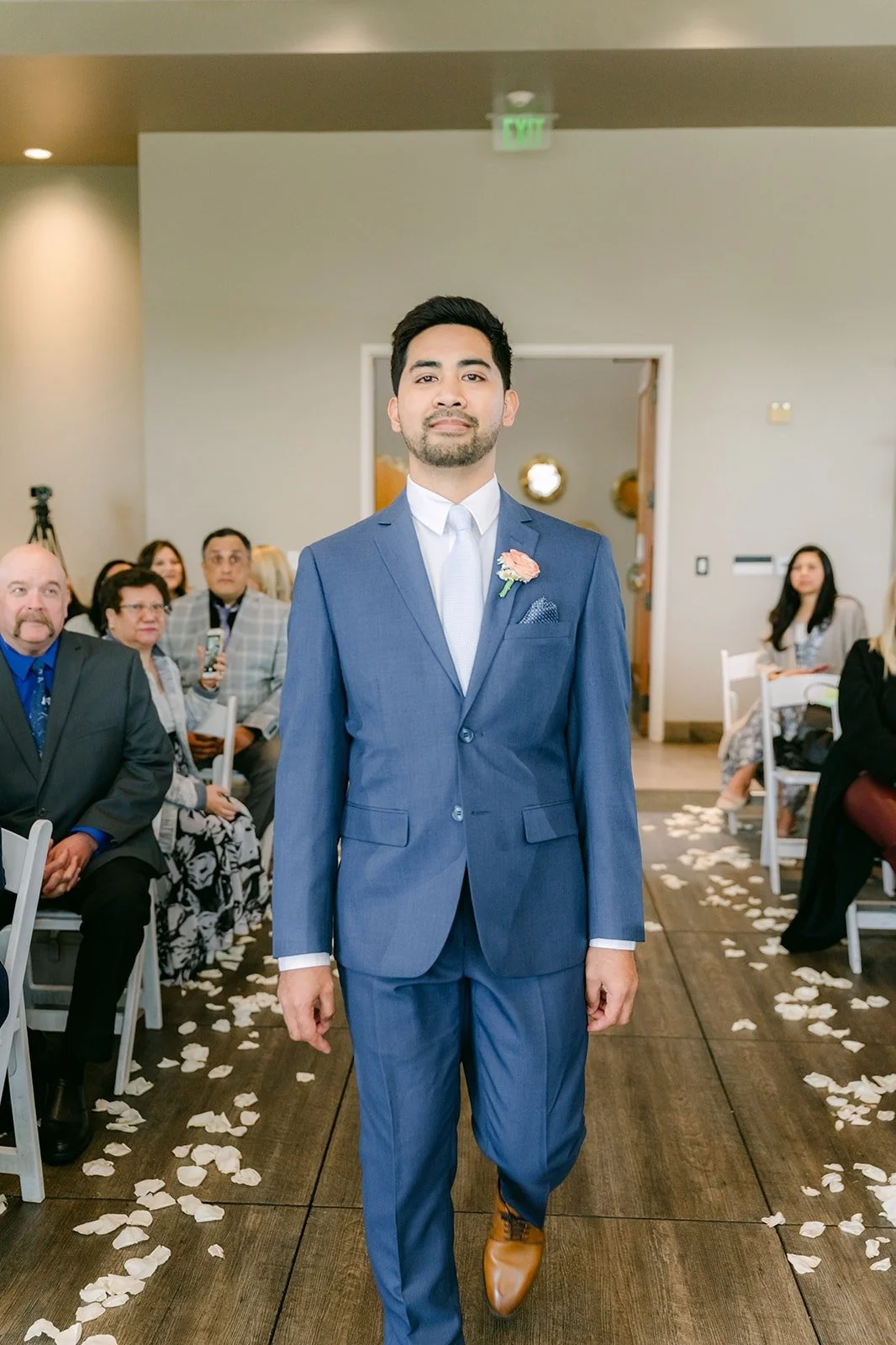 Mark walking down the petal lined aisle in his blue suit