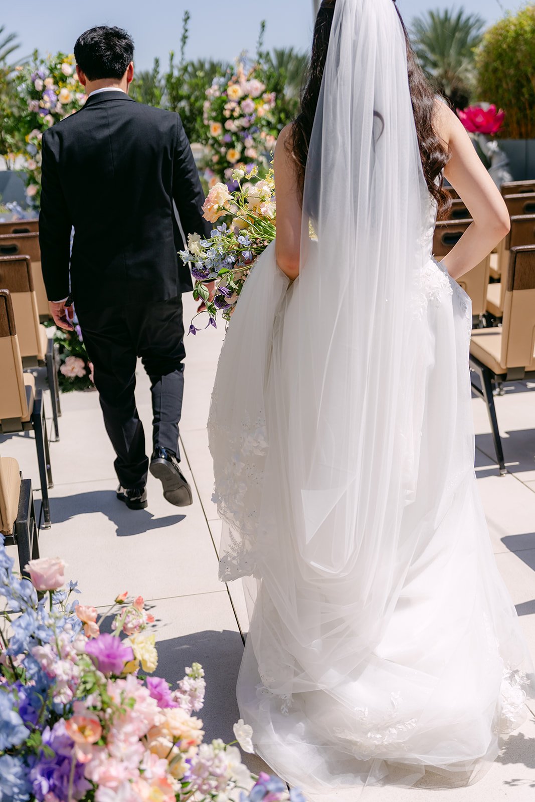Couple walking away down the aisle with her long veil trailing behind