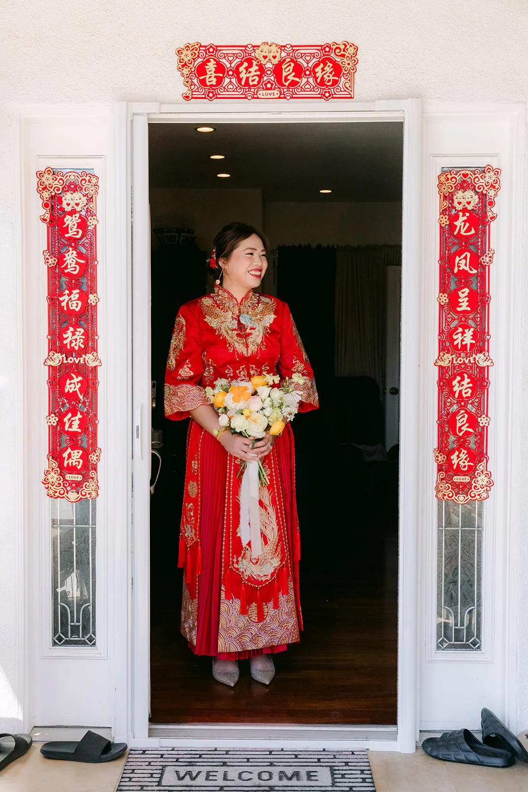 A bride in red standing in a doorway framed by red couplets.
