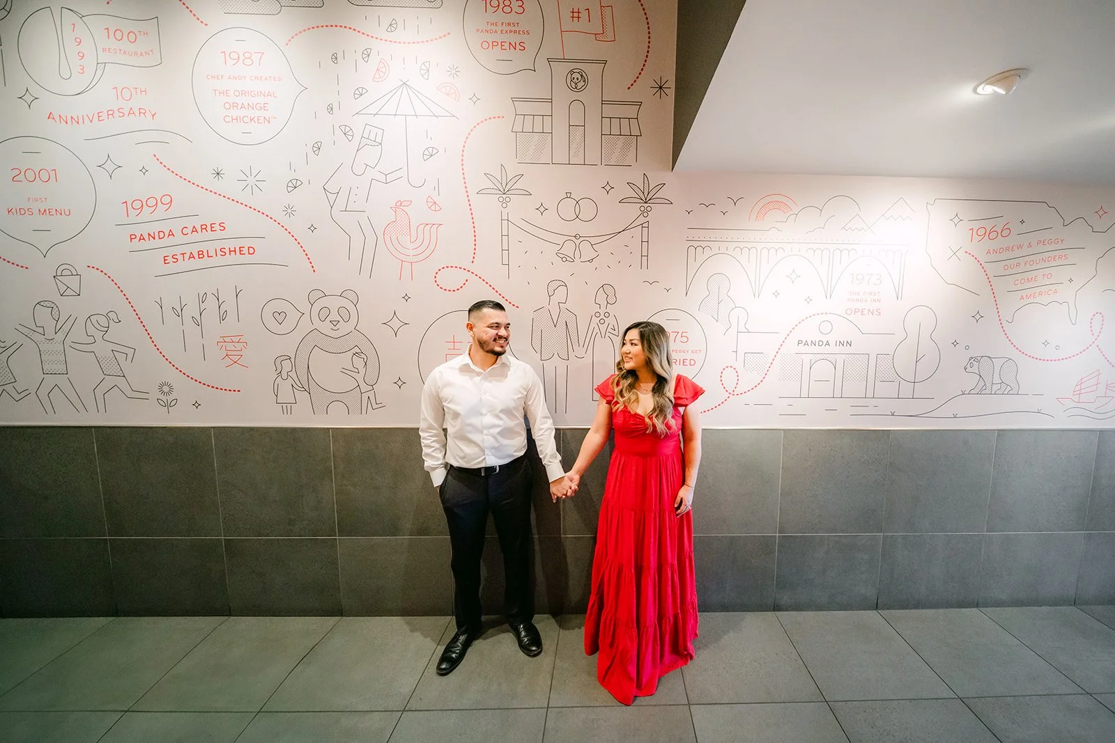 Linh and Ankush hand in hand in front of the restaurant's handwritten mural wall.