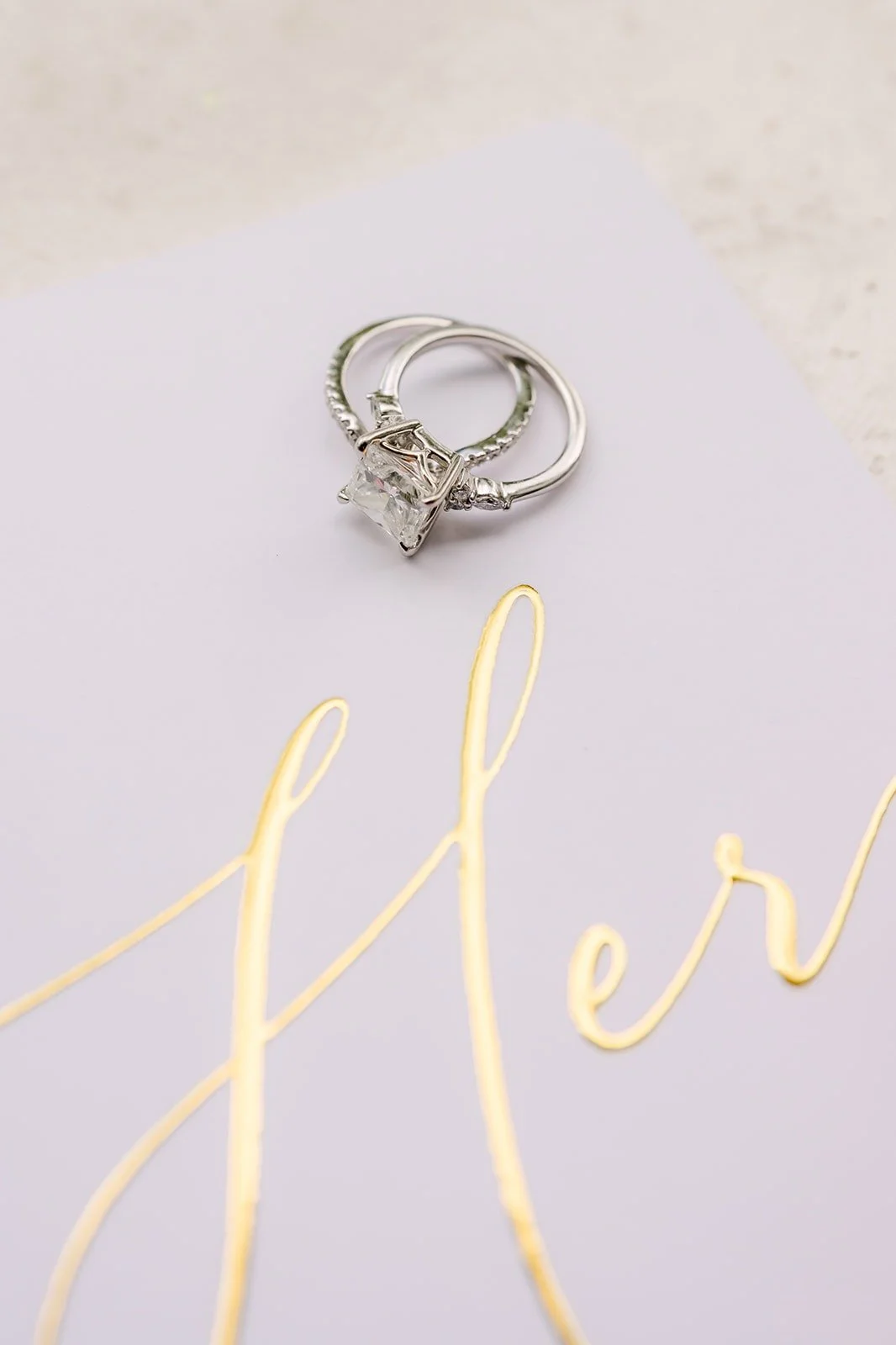 The wedding rings resting on a card lettered "Hers" in gold script