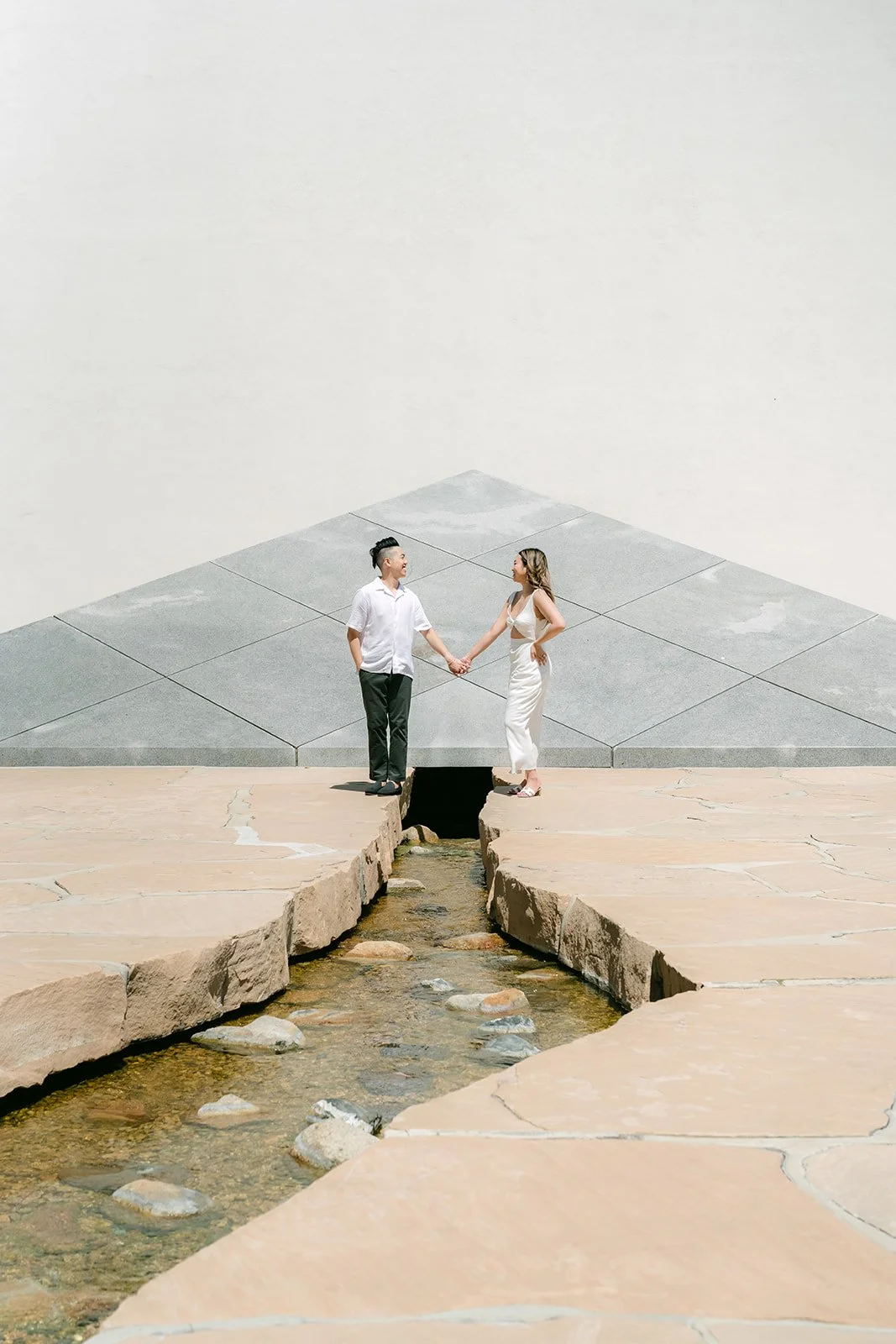 Wide view of the couple at the end of the stone stream in the sculpture garden.