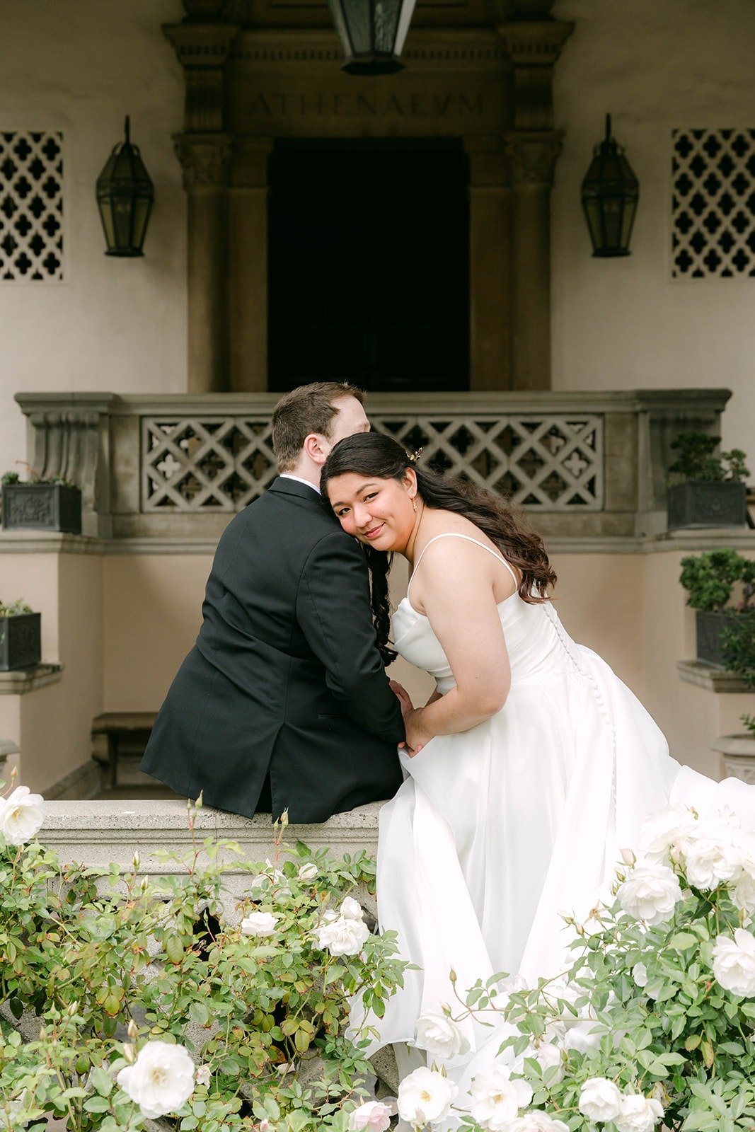 Saira and Matthew sitting close on a low wall in front of the entrance
