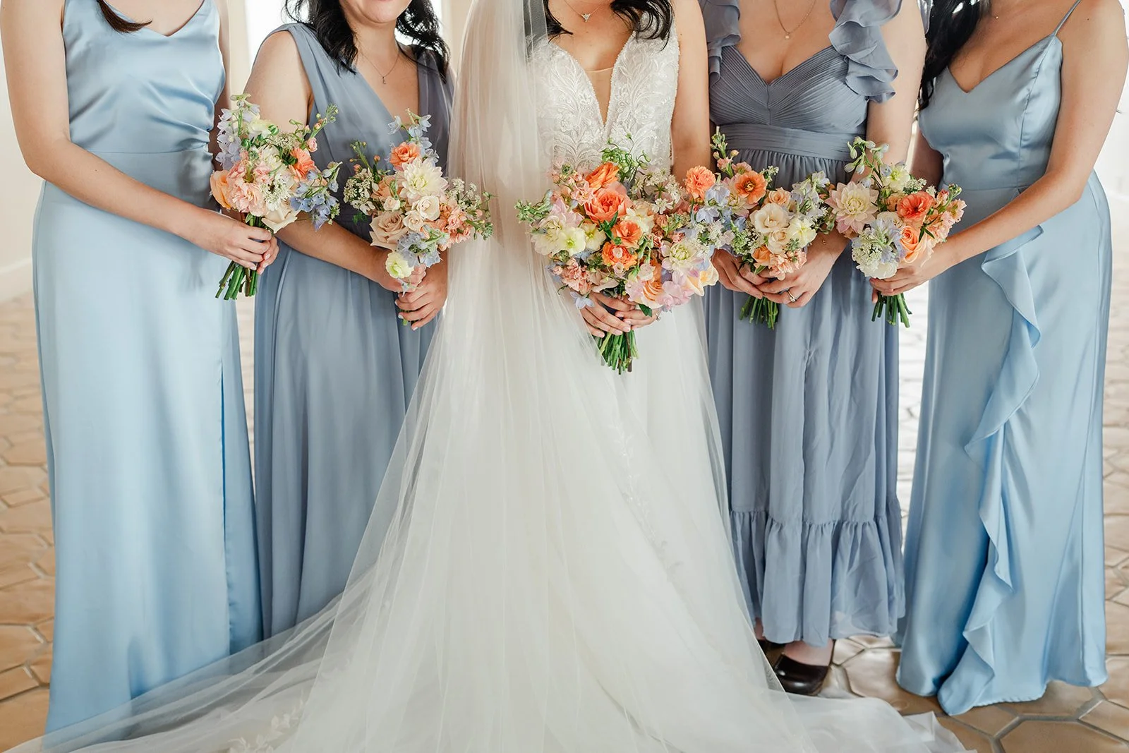 Bouquets held against dusty blue bridesmaid dresses and the bride's gown