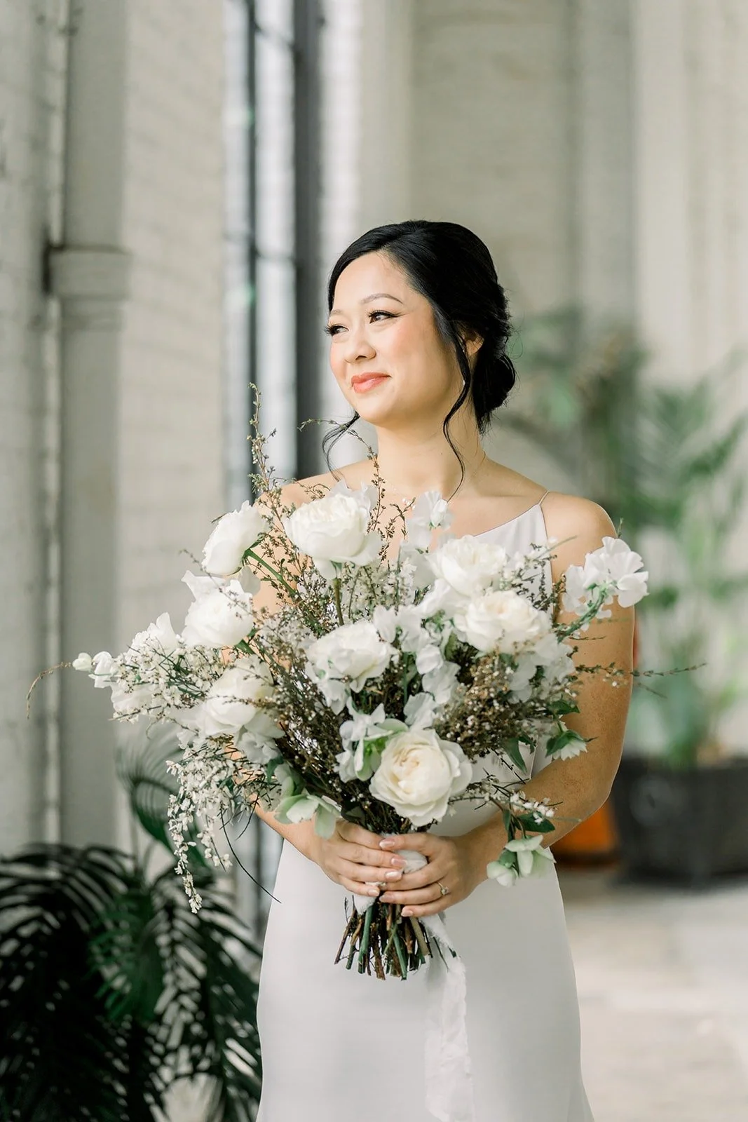Cindy holds her white and green bouquet by the tall windows