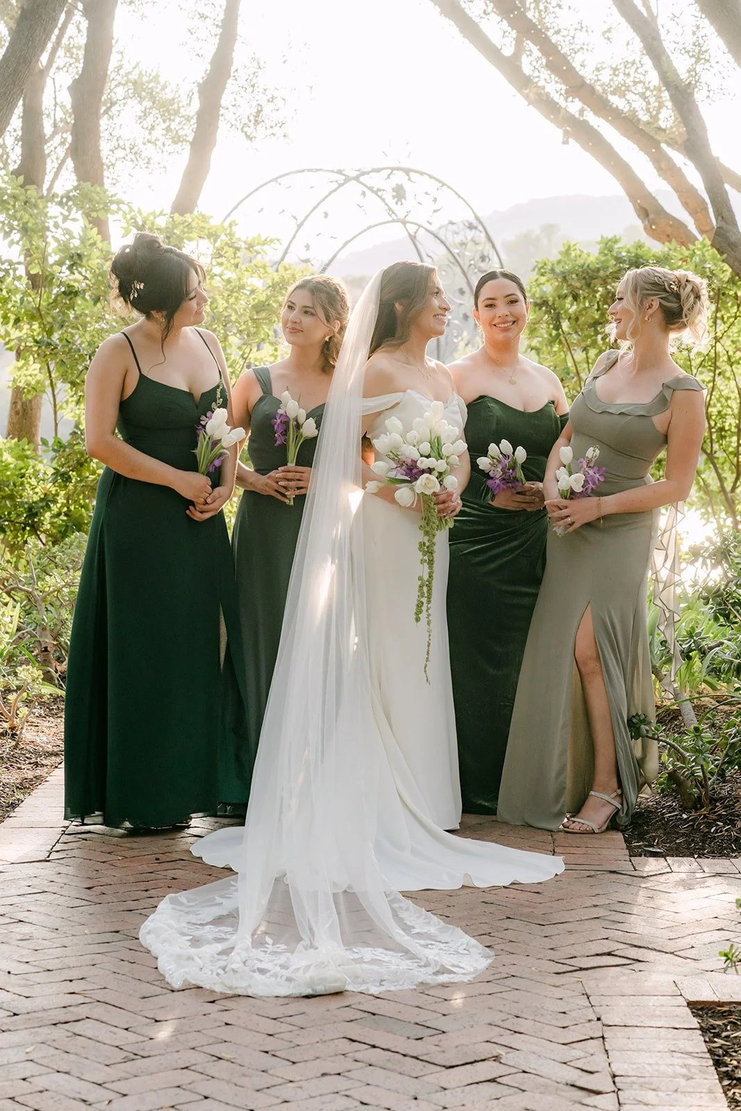 Mariana with her bridesmaids in shades of green under a wrought iron arch