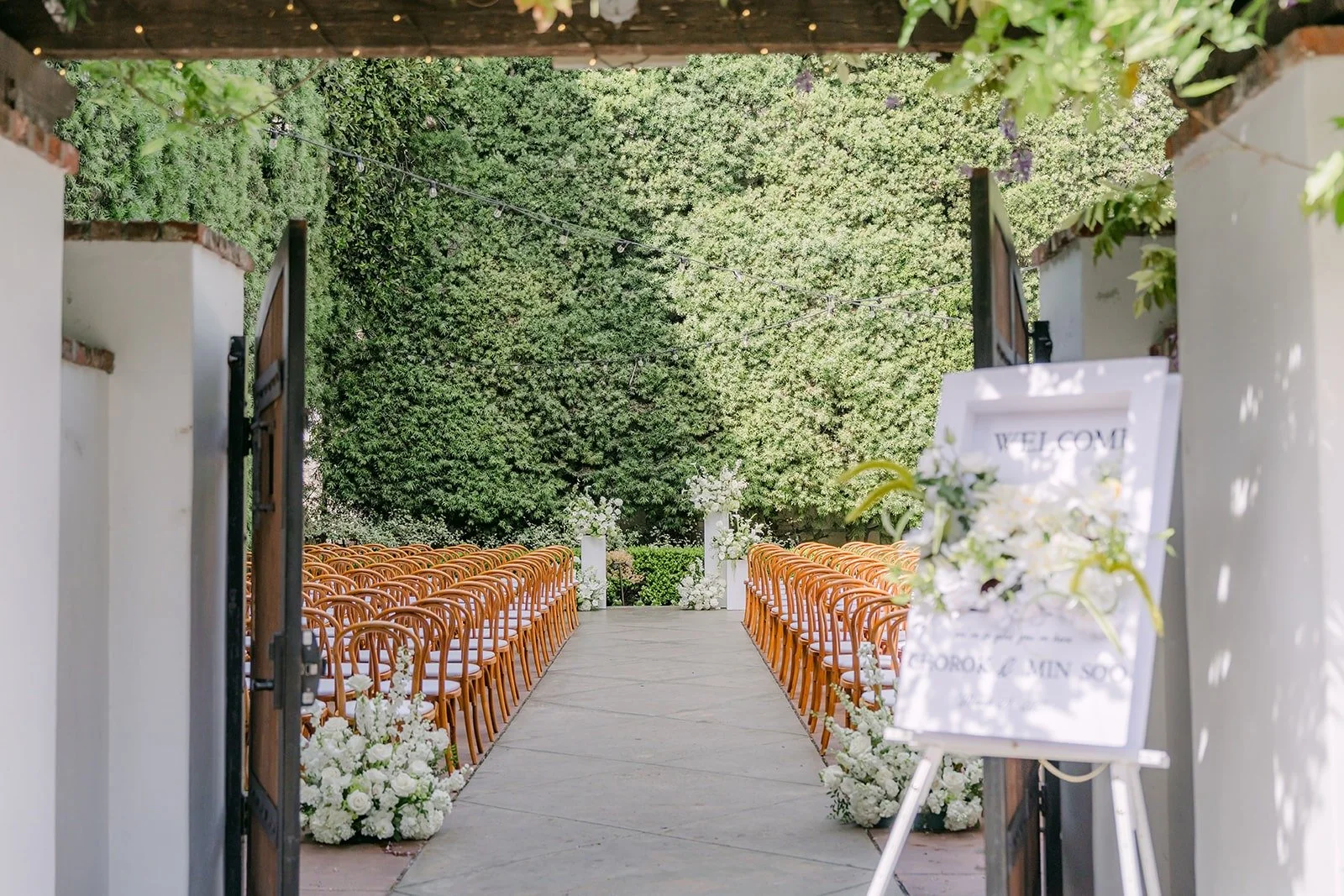 The ceremony entrance at Franciscan Gardens with a welcome sign and rows of wooden chairs beyond