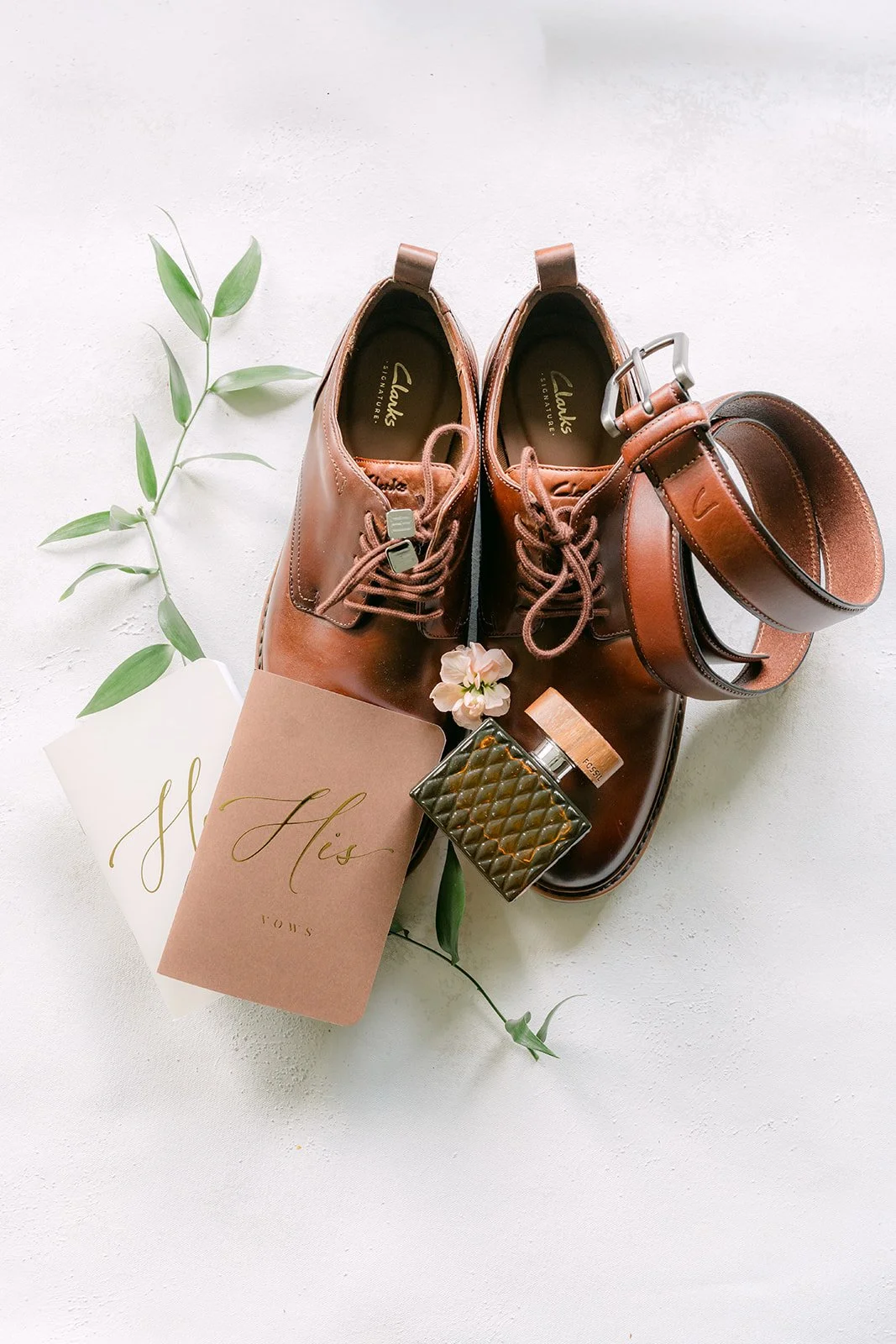 Groom's brown leather shoes and accessories with sprigs of greenery