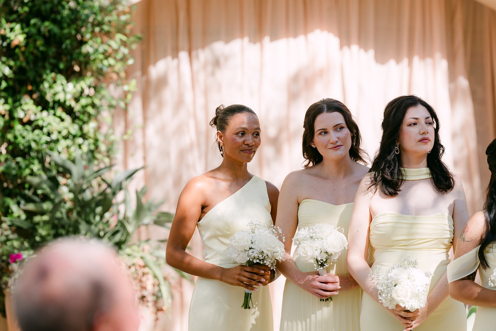 Bridesmaids in butter yellow holding white bouquets at the ceremony