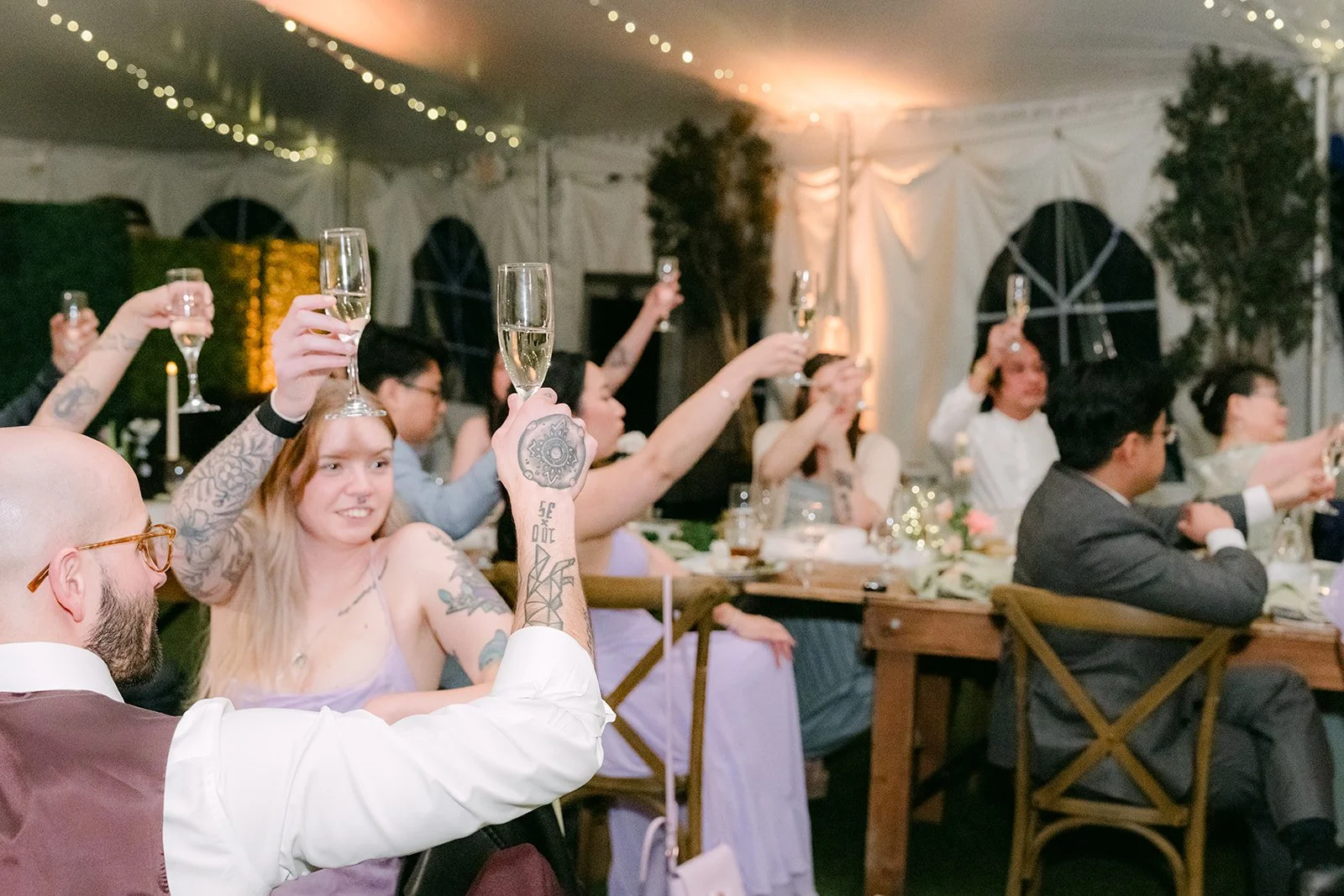 Guests raising their glasses in a toast under string lights