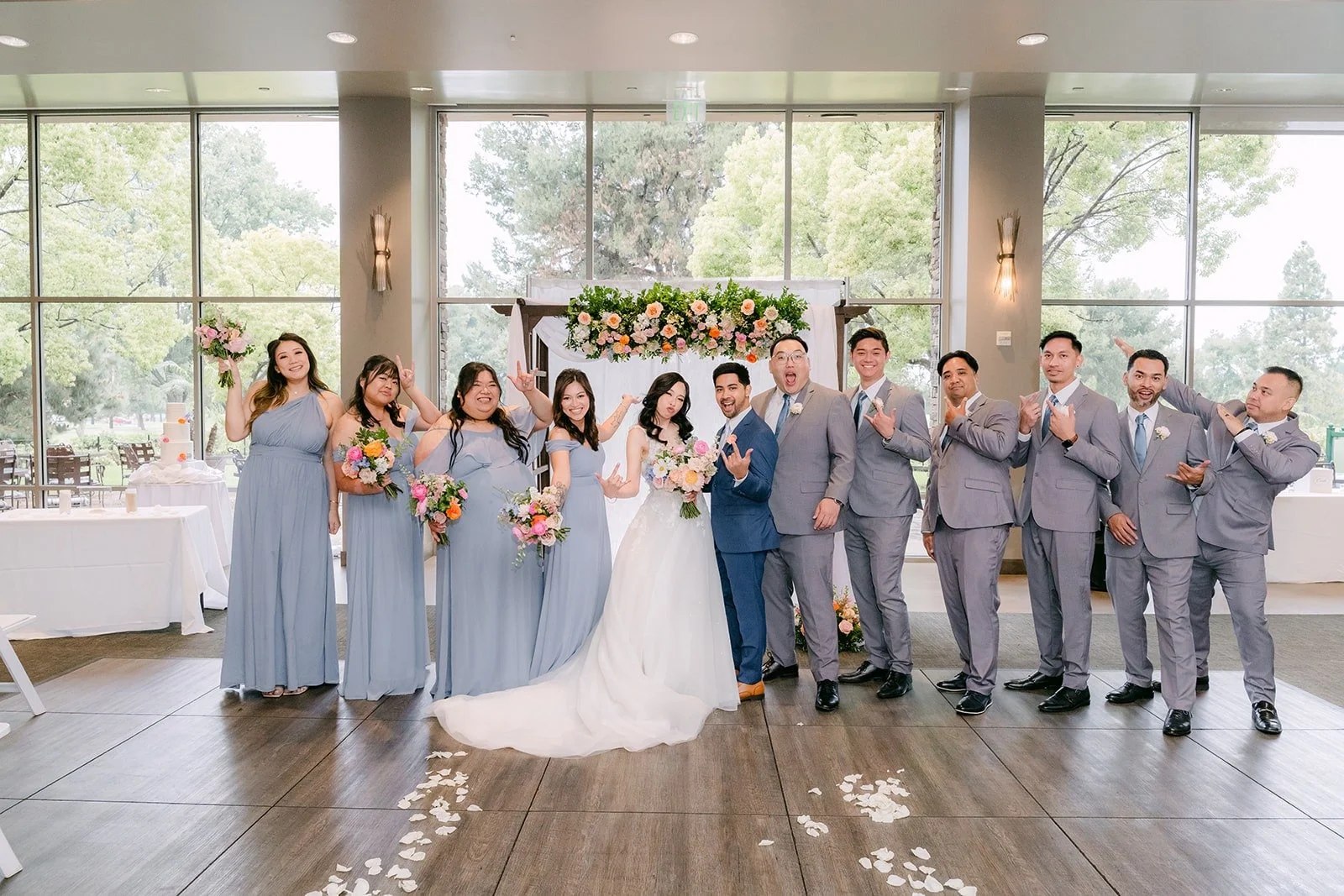 The full wedding party in dusty blue and gray around Natalie and Mark at the arch