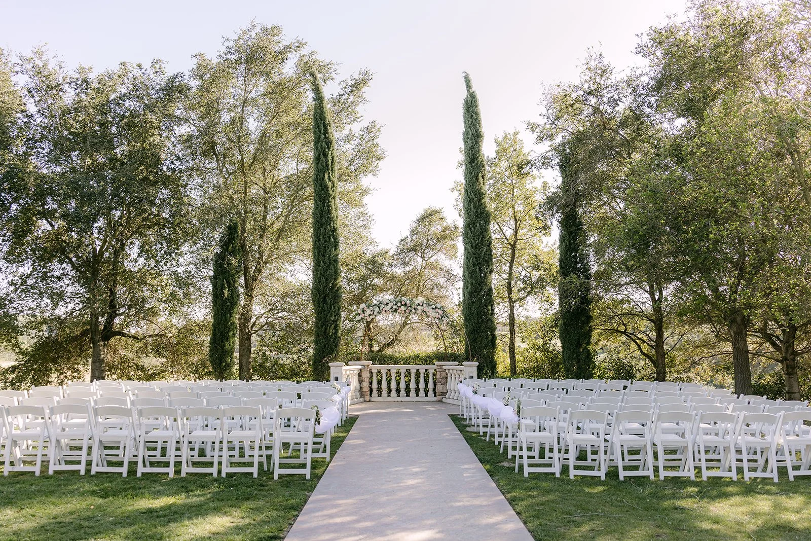 Ceremony lawn at Vellano Estate with white chairs lining the aisle and cypress trees