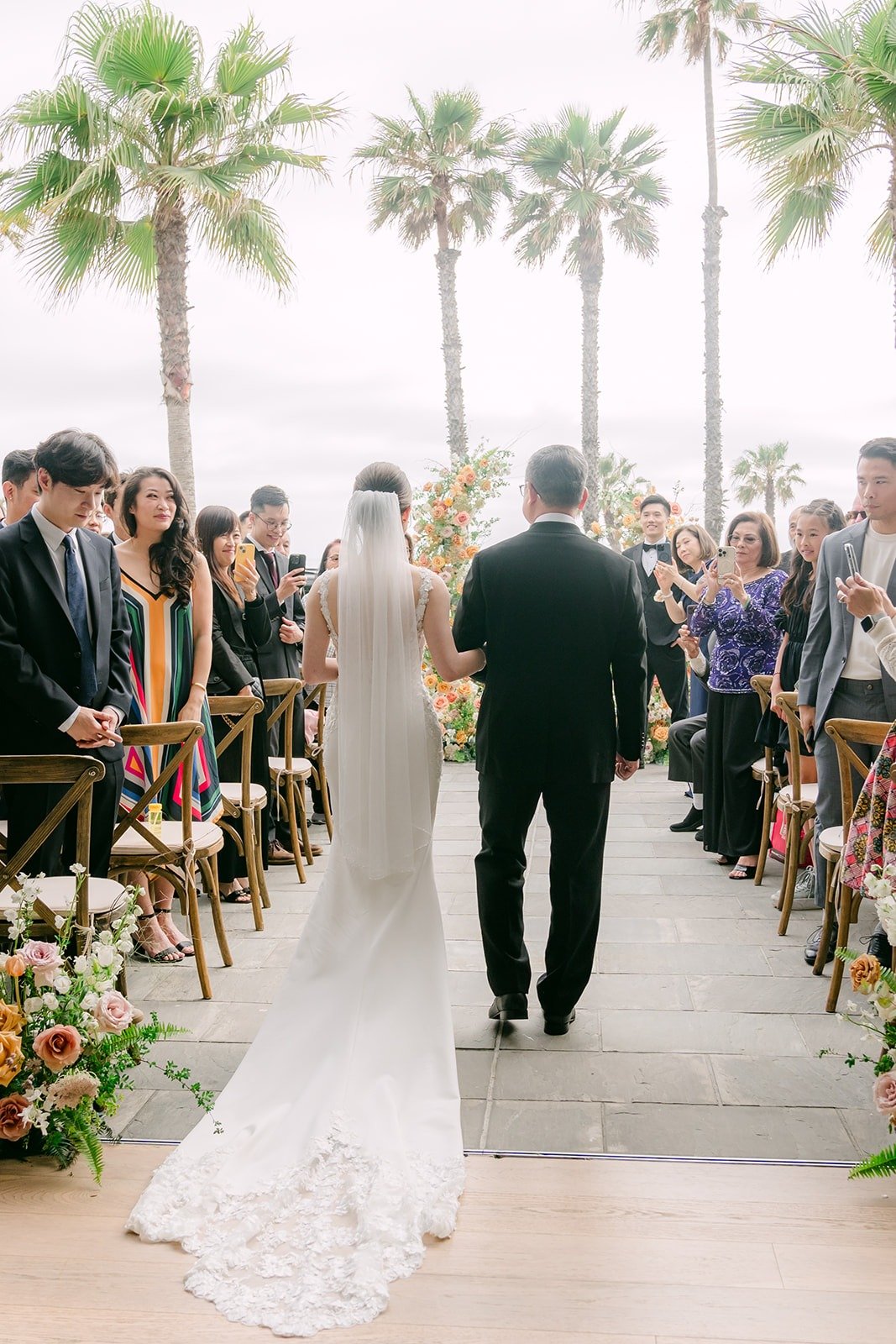 Angela walking down the aisle toward Eli with her lace train behind her