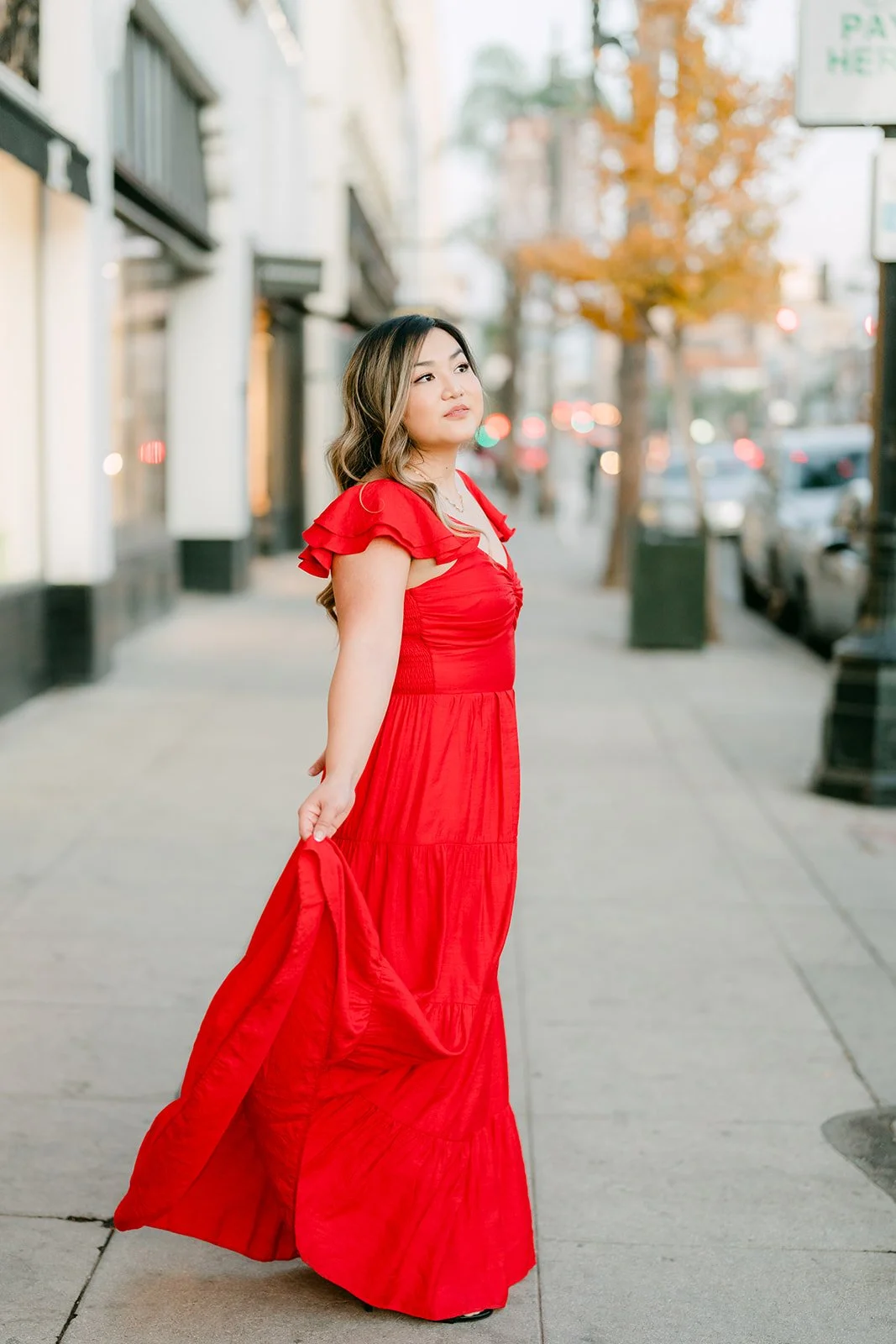 Linh in her red dress walking along an Old Town Pasadena sidewalk, photographed by One and Only Production.