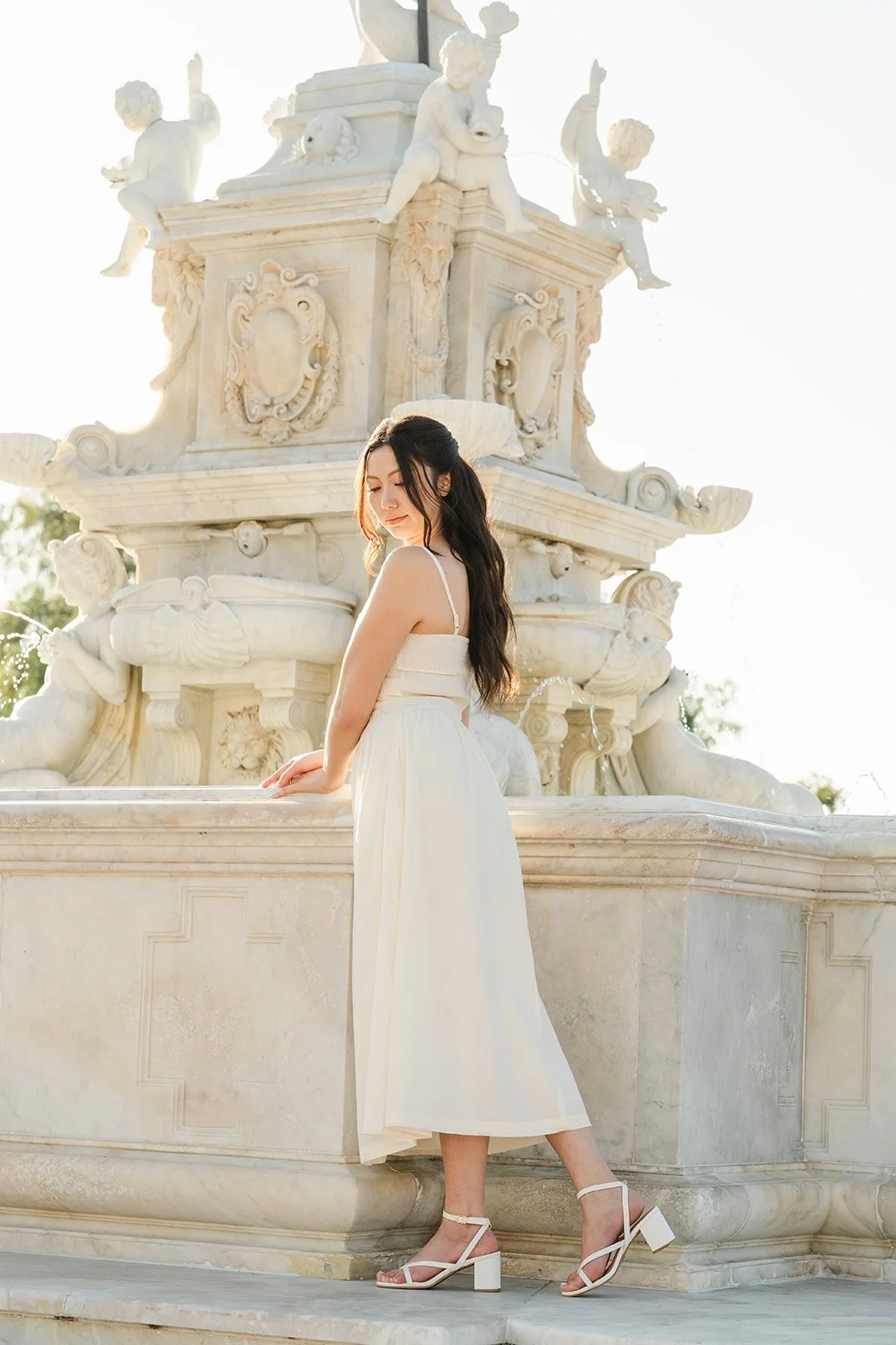 Victoria stands in her white dress beside the fountain.