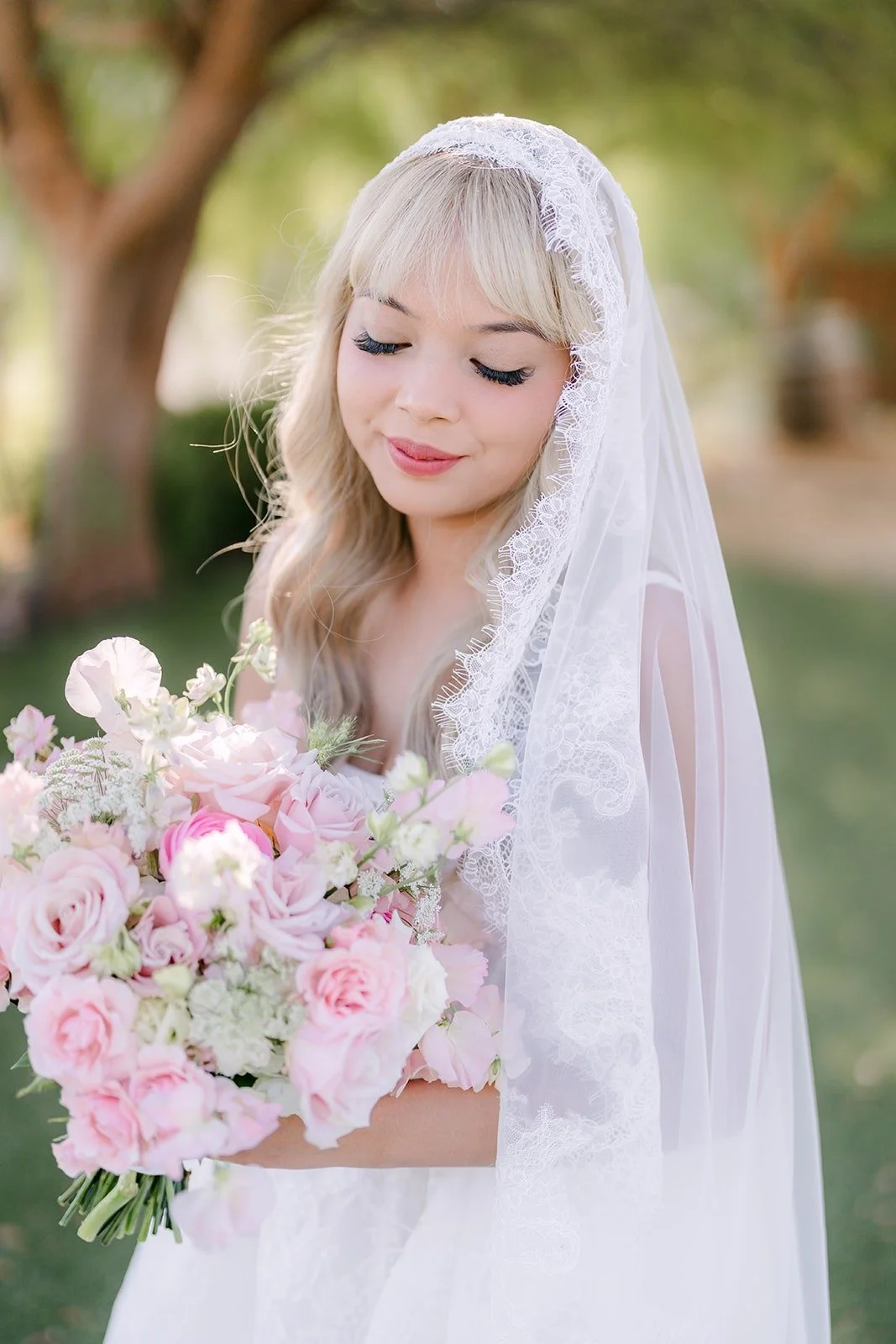 Konitha holding her blush rose bouquet under the trees